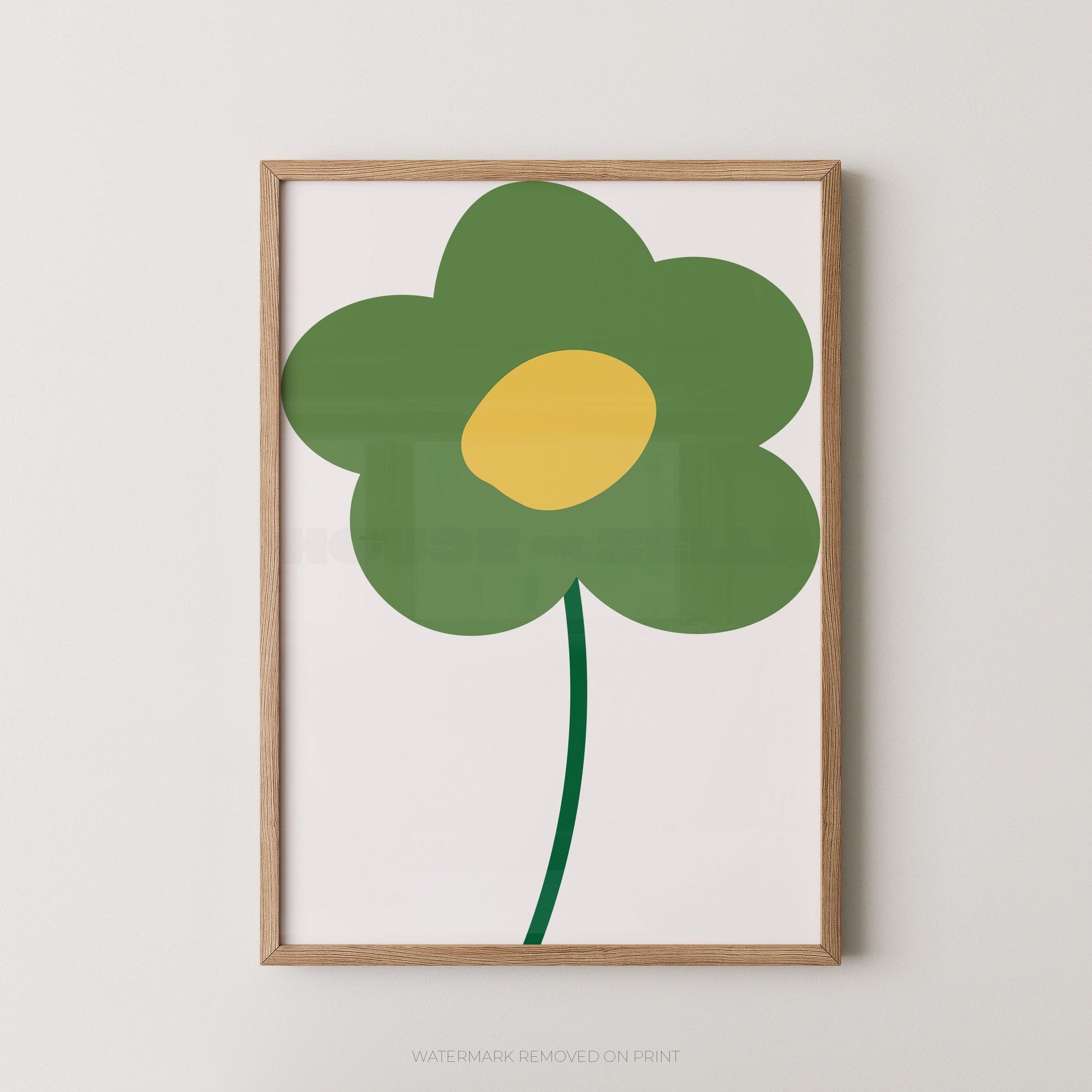 A framed minimalist art print featuring a stylized green flower with a yellow center on a white background, enclosed in a light natural wood frame against a neutral light gray wall.