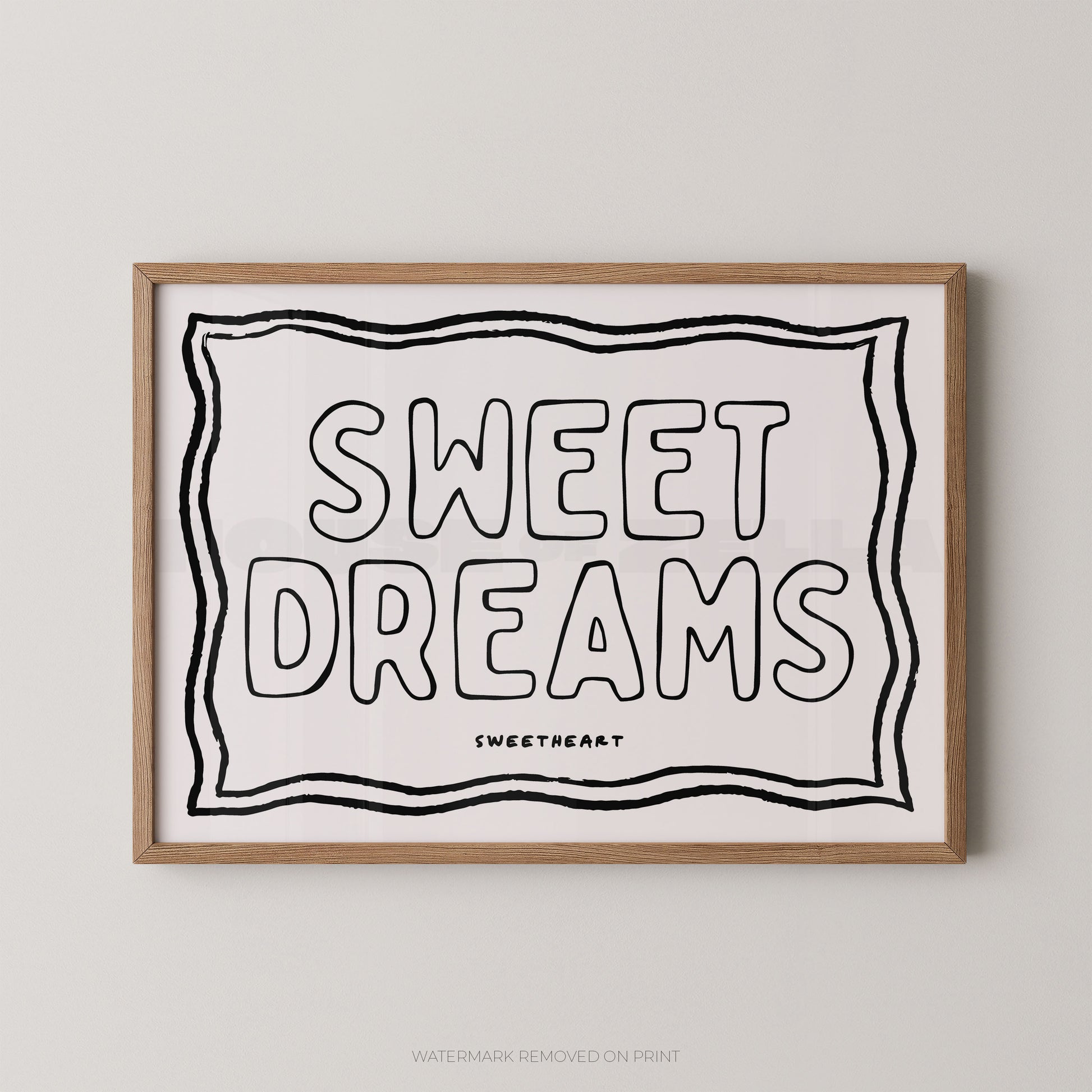 A framed typographic wall art print with the words “SWEET DREAMS” in large outlined letters on a white background, bordered by black wavy lines, with “SWEETHEART” printed below. The print is shown in a light natural wood frame against a light gray wall.