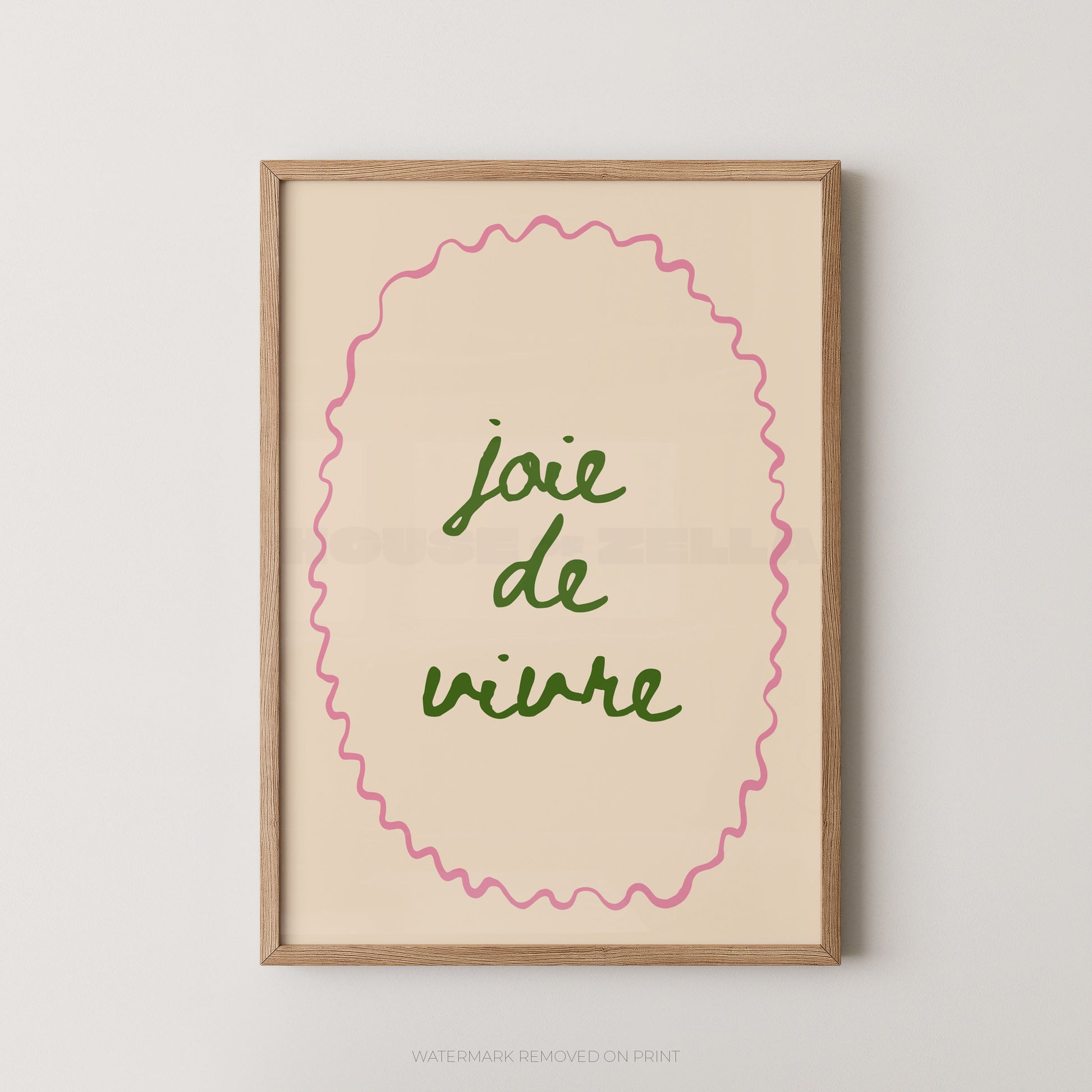 Framed wall art print with the French phrase “joie de vivre” in green script inside a pink wavy oval border, set in a light wood frame against a light gray wall.