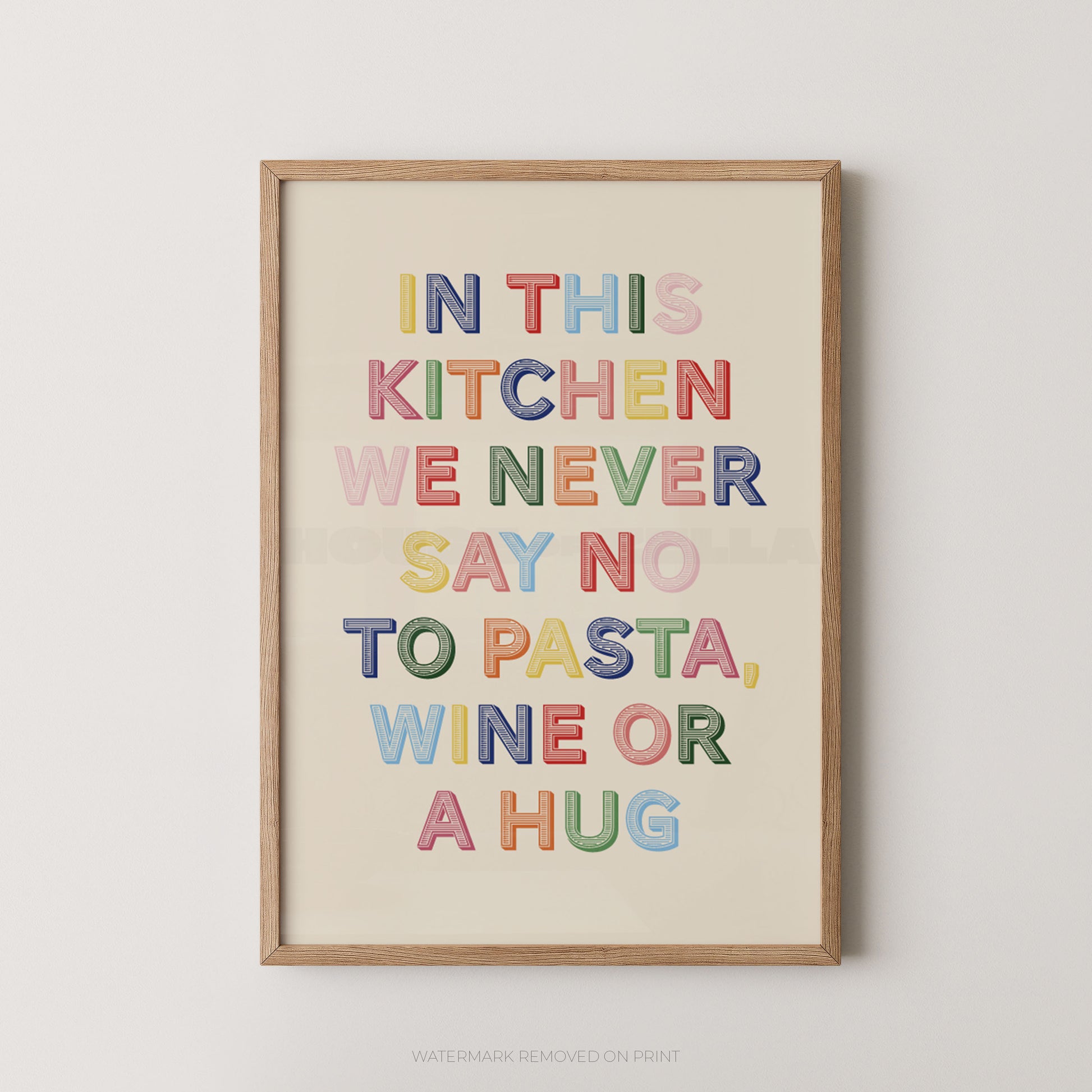A framed typographic wall art print with the phrase “IN THIS KITCHEN WE NEVER SAY NO TO PASTA, WINE OR A HUG” in colorful block letters on a cream background, shown hanging against a light neutral wall.