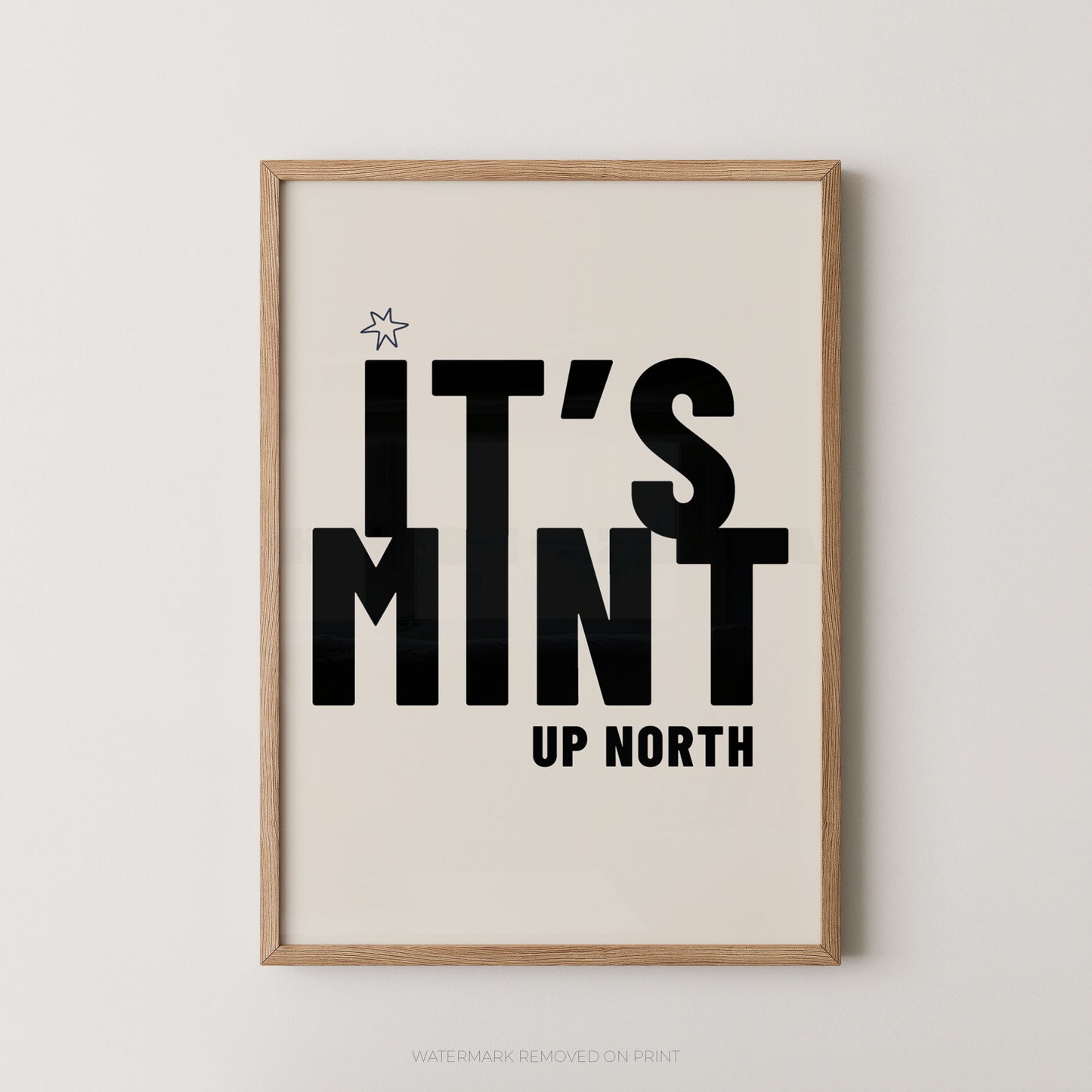 Framed typographic wall art reading “IT’S MINT UP NORTH” in bold black text on a warm off-white background, shown in a light natural wood frame against a light neutral wall.