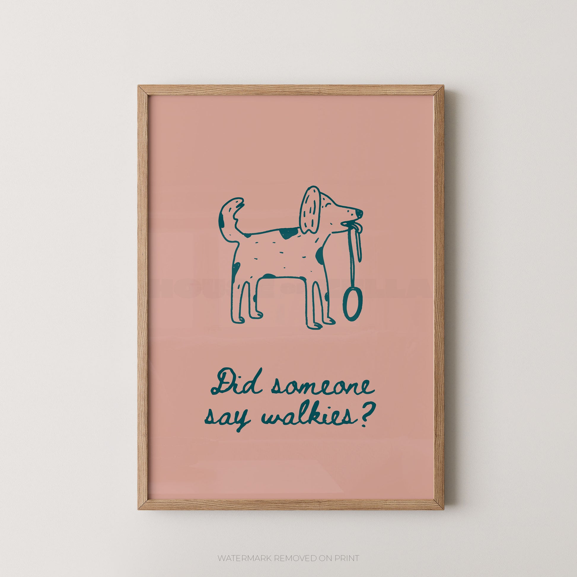A framed art print featuring a simple blue line drawing of a dog holding a leash on a dusty pink background, with the text 'Did someone say walkies?' below. The print is housed in a light natural wood frame and is displayed against a neutral light gray wall.