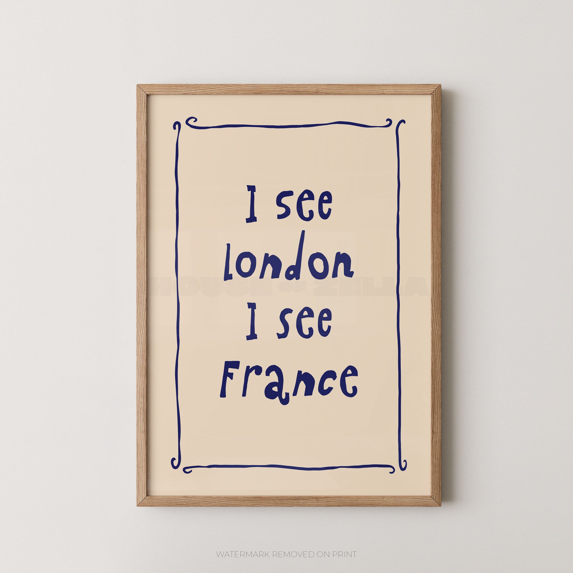 Framed typographic wall art hanging on a light neutral wall. The print has a cream background with dark blue handwritten-style text reading 'I see London I see France' inside a thin blue decorative border, surrounded by a light natural wood frame.