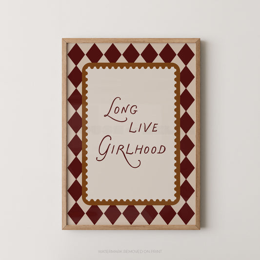 A framed typographic wall art print with the words “Long Live Girlhood” in dark red script, surrounded by a cream center panel and a dark red diamond pattern border, mounted on a light neutral wall.
