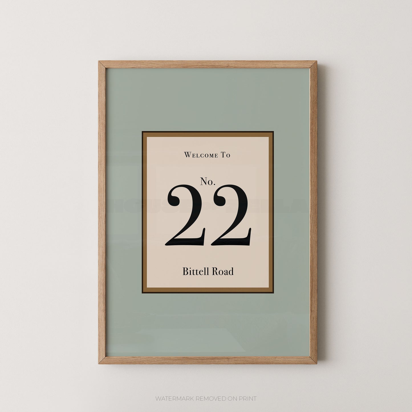 Framed wall art print with a sage green mat and a light wood frame, featuring a central cream panel with the text 'WELCOME TO No. 22 Bitell Road' in black serif lettering.