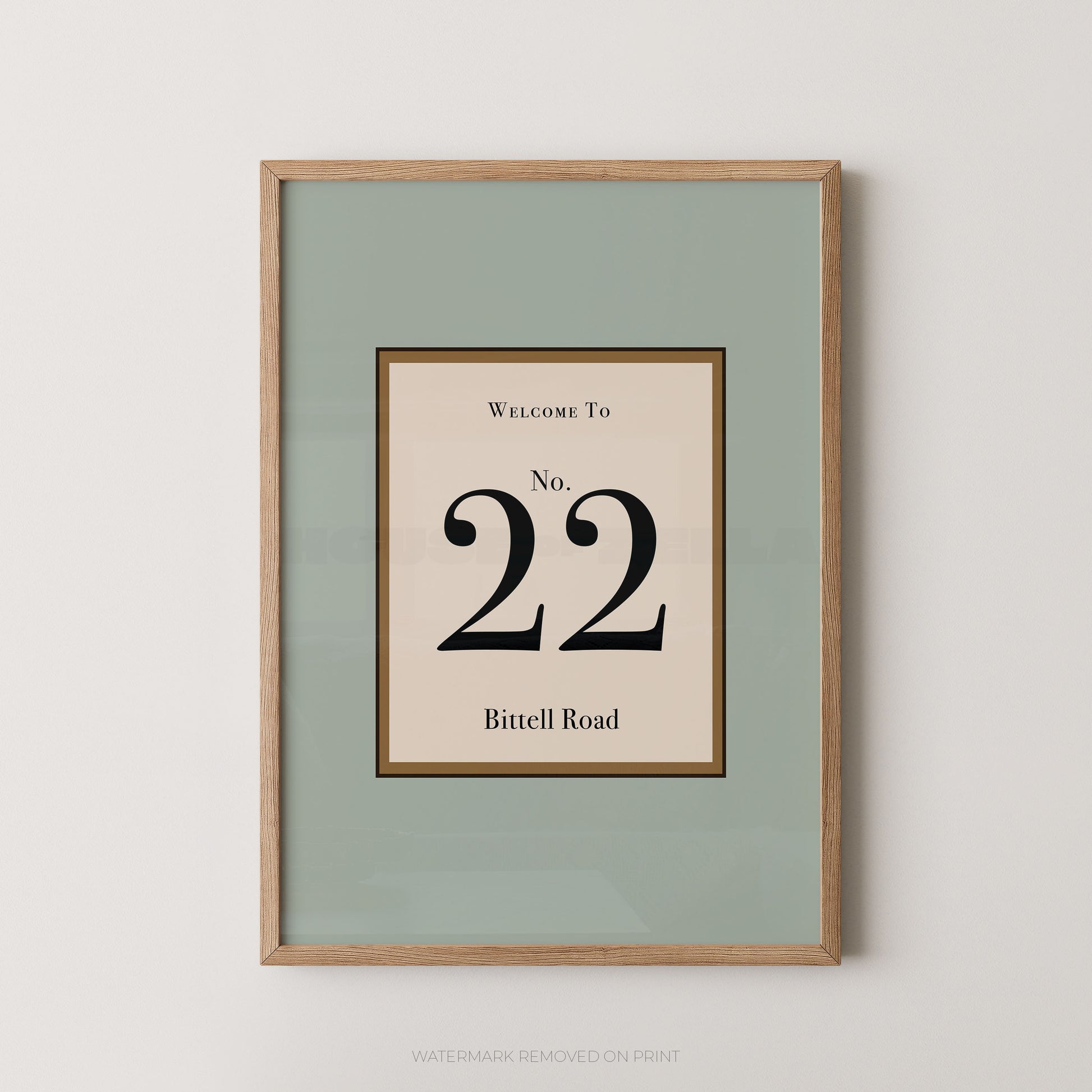 Framed wall art print with a sage green mat and a light wood frame, featuring a central cream panel with the text 'WELCOME TO No. 22 Bitell Road' in black serif lettering.