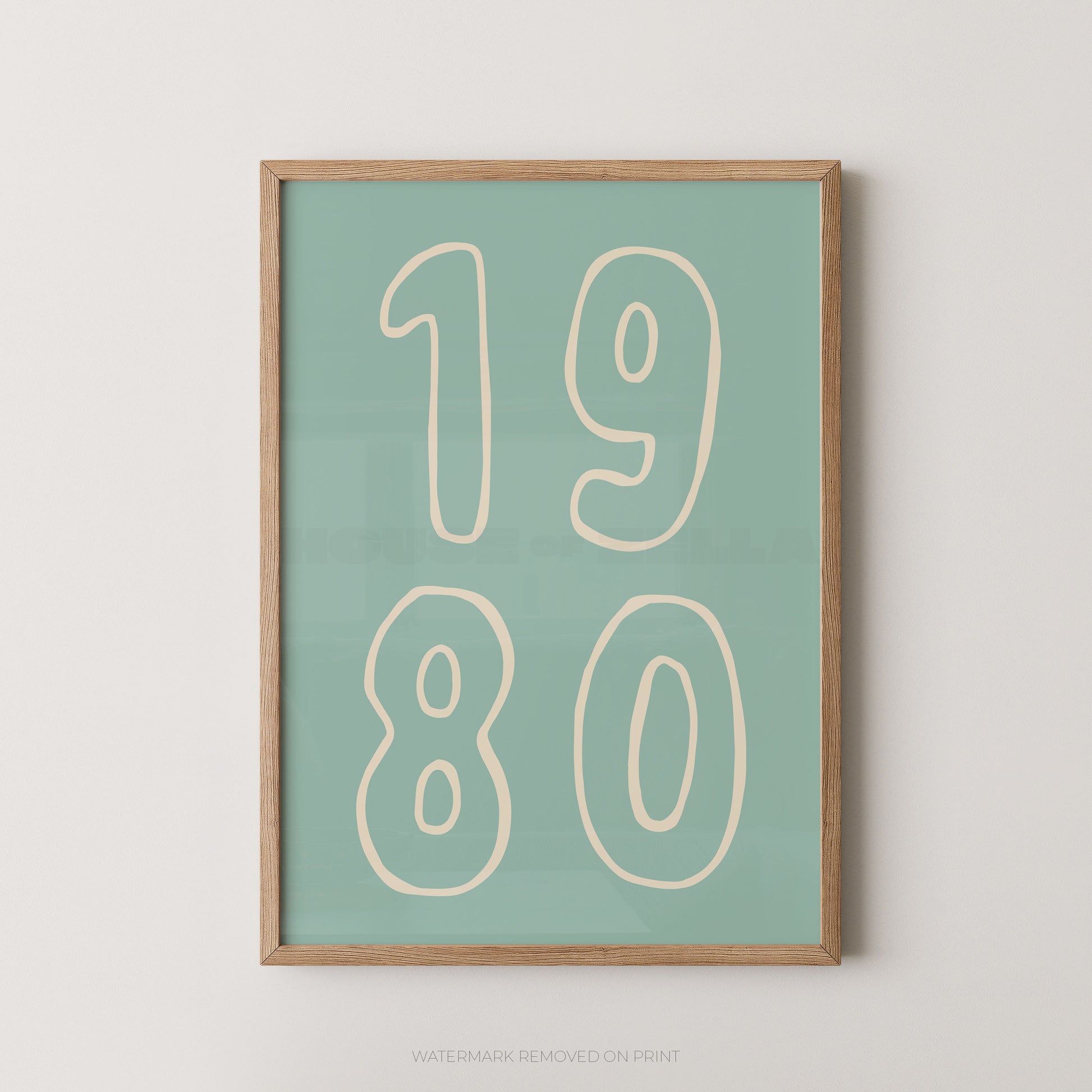 A framed minimalist art print featuring the numbers '1980' in cream outline font on a muted teal-green background, enclosed in a light natural wood frame against a light gray wall.
