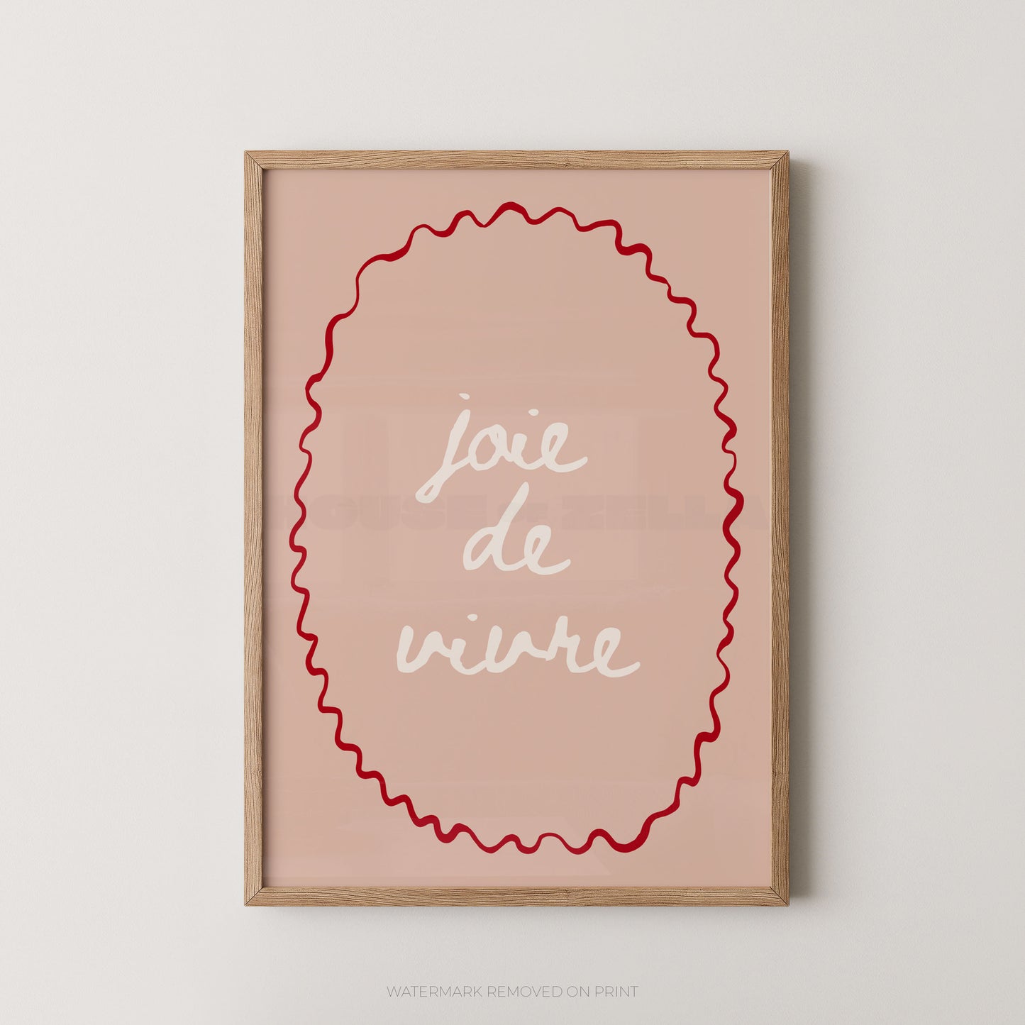 Framed wall art print with the French phrase “joie de vivre” in white script inside a red wavy oval, set in a light wood frame against a plain light gray wall.