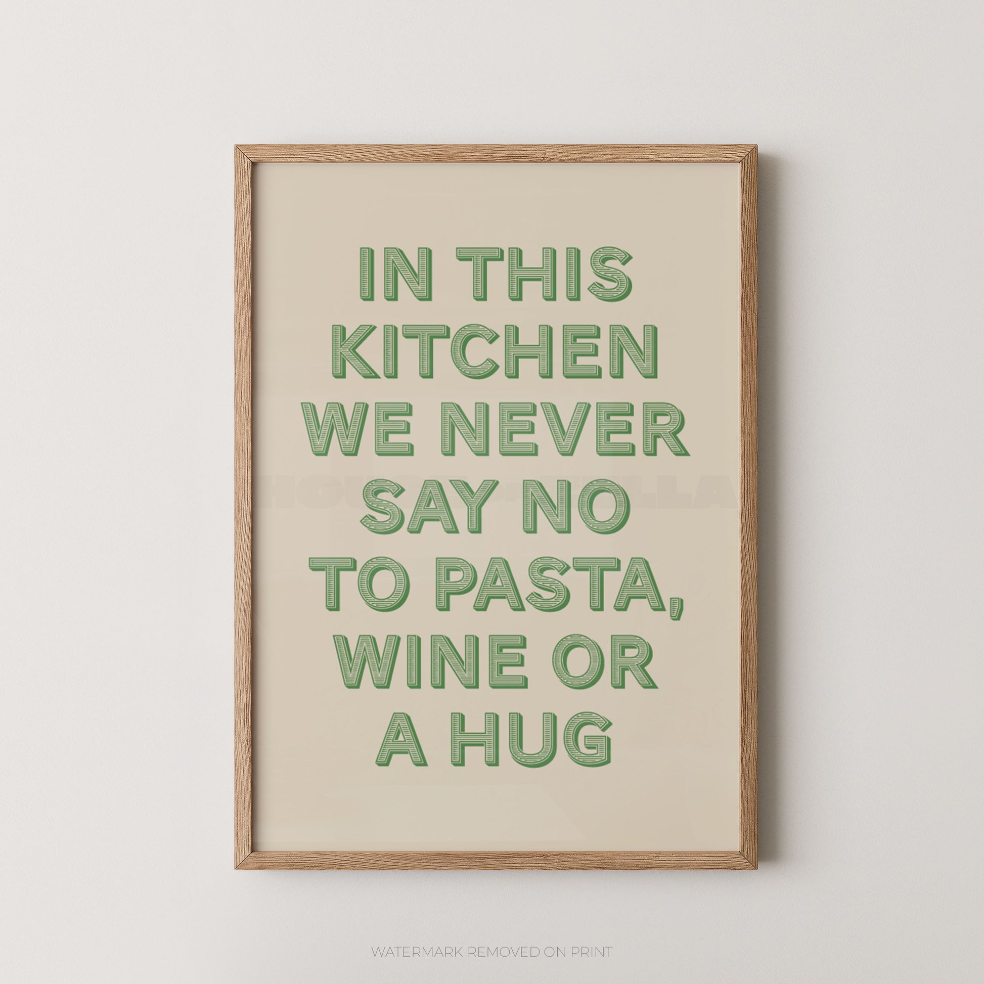 A framed typographic wall art print with the phrase “IN THIS KITCHEN WE NEVER SAY NO TO PASTA, WINE OR A HUG” in muted green letters on a warm cream background, shown in a light natural wood frame against a light gray wall.