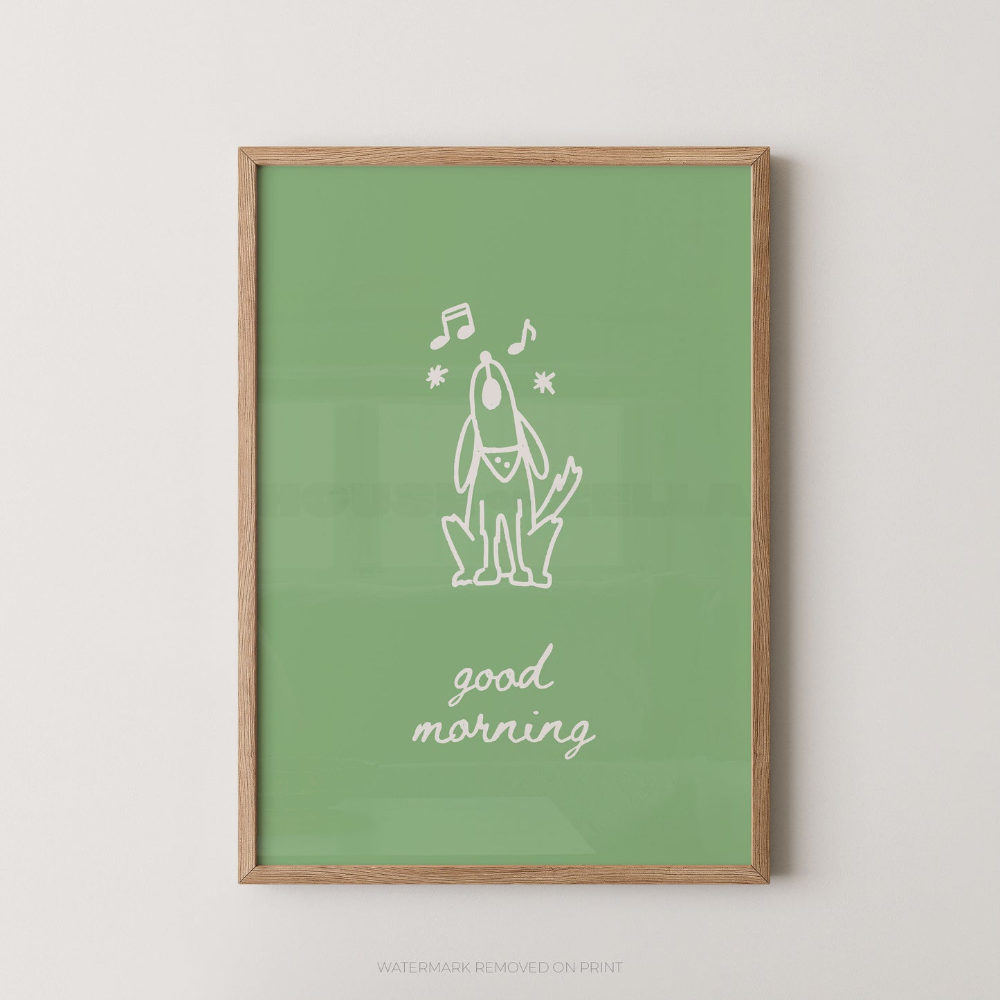 A framed art print featuring a minimalist white line drawing of a dog with musical notes and the text 'good morning' on a sage green background, enclosed in a light wood frame against a neutral light gray wall.