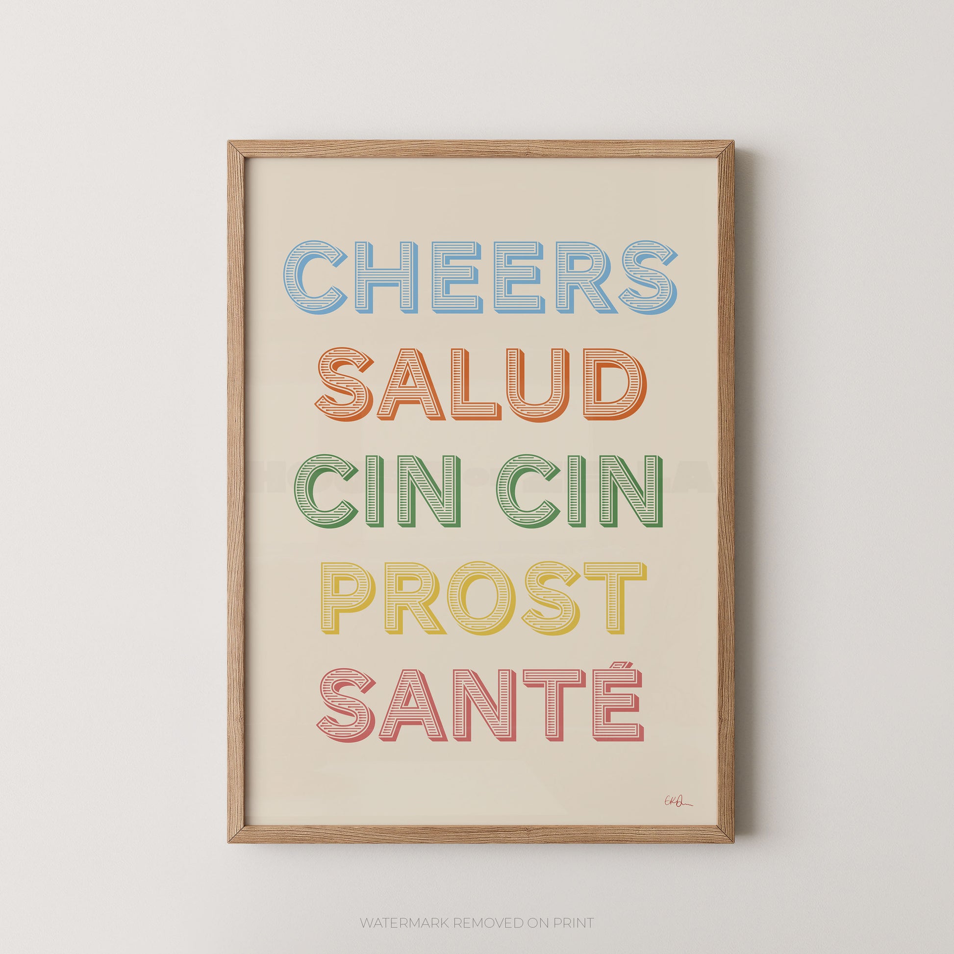 Framed typographic wall art with the phrase 'CHEERS SALUD CIN CIN PROST SANTÉ' in pastel multicolor letters on a cream background, shown hanging against a light neutral wall.