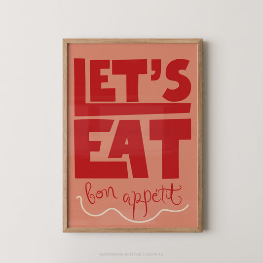 Framed typographic wall art with the words “LET’S EAT bon appetit” in red lettering on a peach background, shown hanging against a light neutral wall.