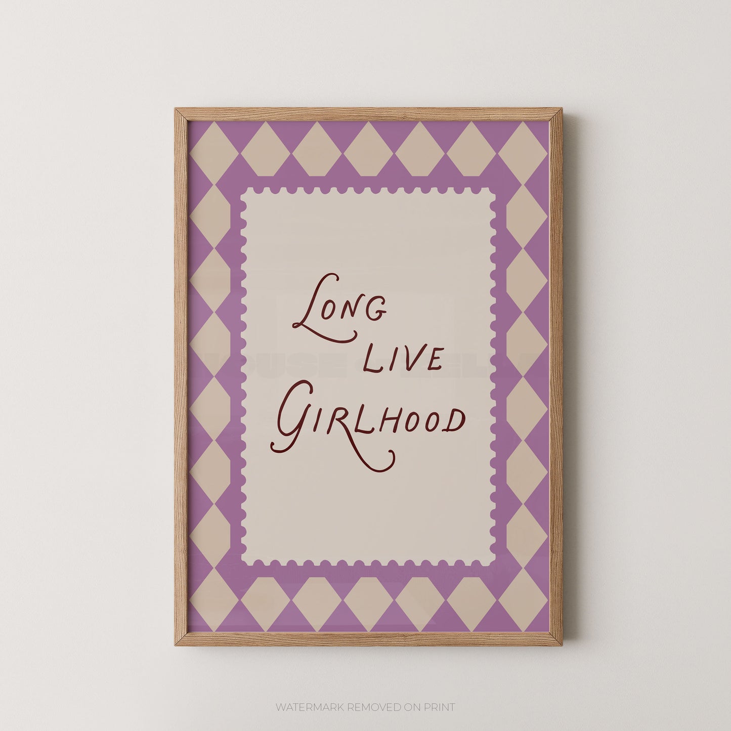 A framed typographic wall art print with the phrase “Long Live Girlhood” in dark script on an off-white center panel, surrounded by a lavender and cream harlequin diamond border and a light wood frame, shown against a plain light wall.