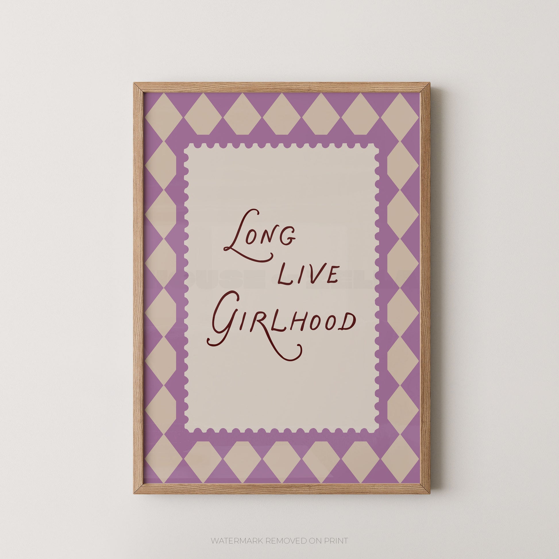 A framed typographic wall art print with the phrase “Long Live Girlhood” in dark script on an off-white center panel, surrounded by a lavender and cream harlequin diamond border and a light wood frame, shown against a plain light wall.
