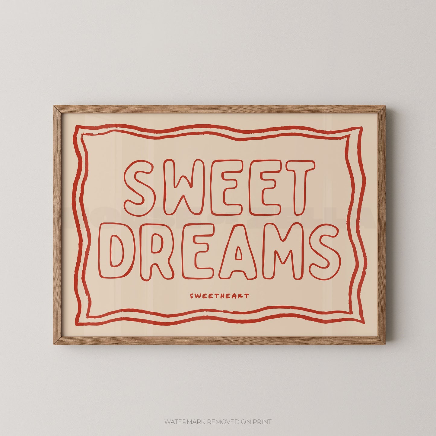 A framed typographic wall art print with the words “SWEET DREAMS” in red outline lettering on a warm cream background, enclosed in a light natural wood frame and shown against a light gray wall.