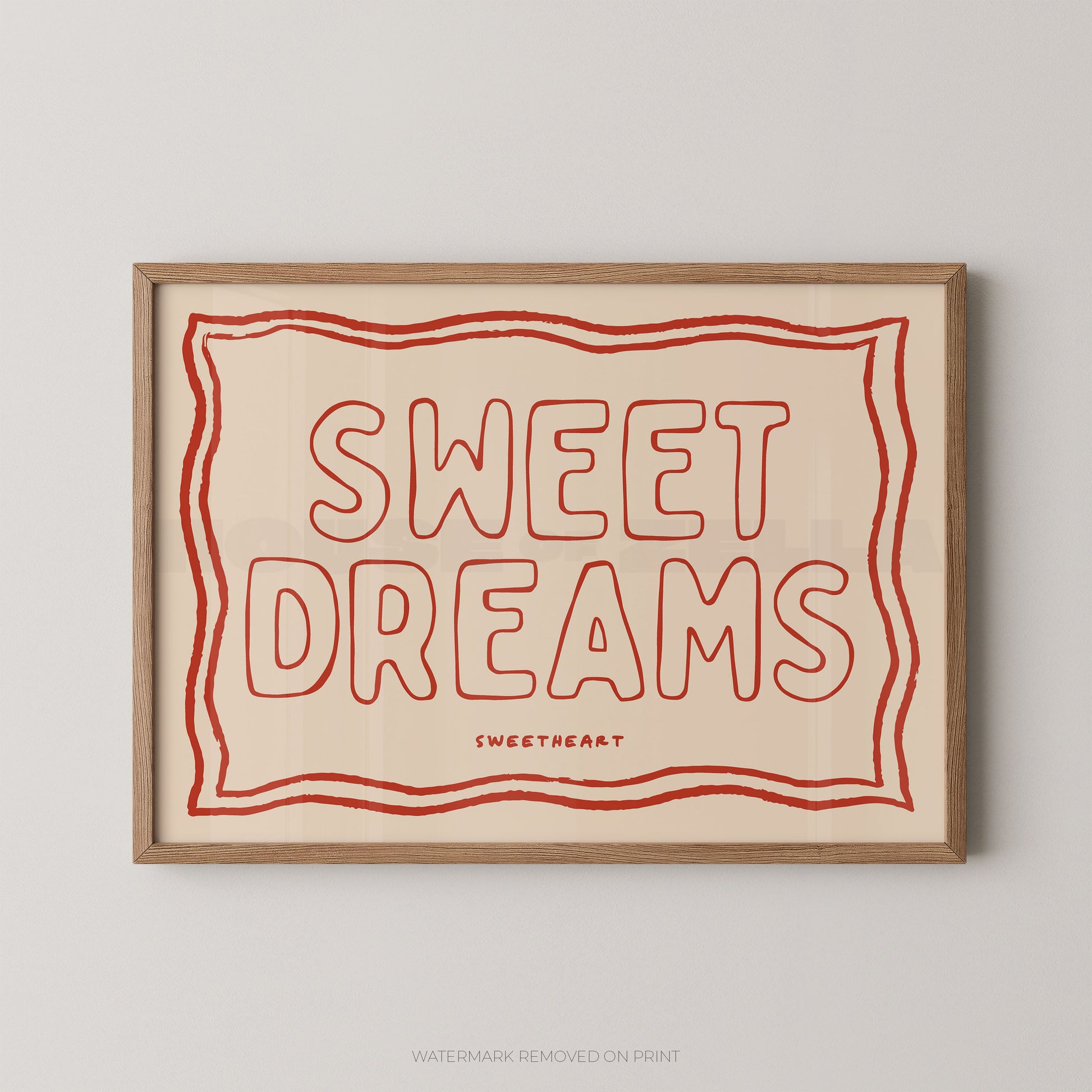 A framed typographic wall art print with the words “SWEET DREAMS” in red outline lettering on a warm cream background, enclosed in a light natural wood frame and shown against a light gray wall.