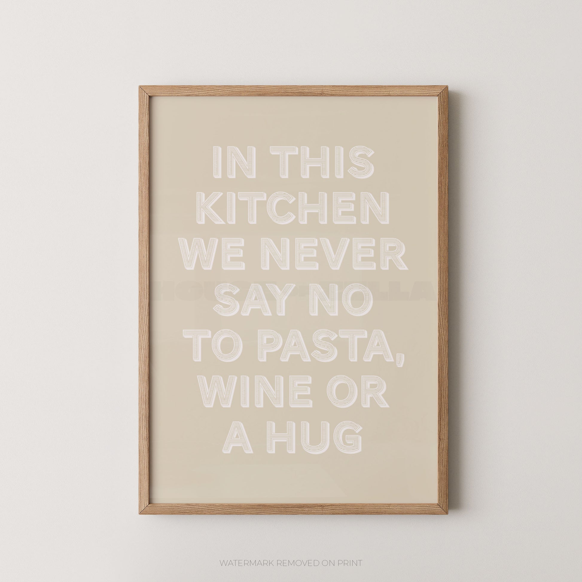 A framed typographic wall art print with the phrase “IN THIS KITCHEN WE NEVER SAY NO TO PASTA, WINE OR A HUG” in large white letters on a warm beige background, shown hanging against a light neutral wall.