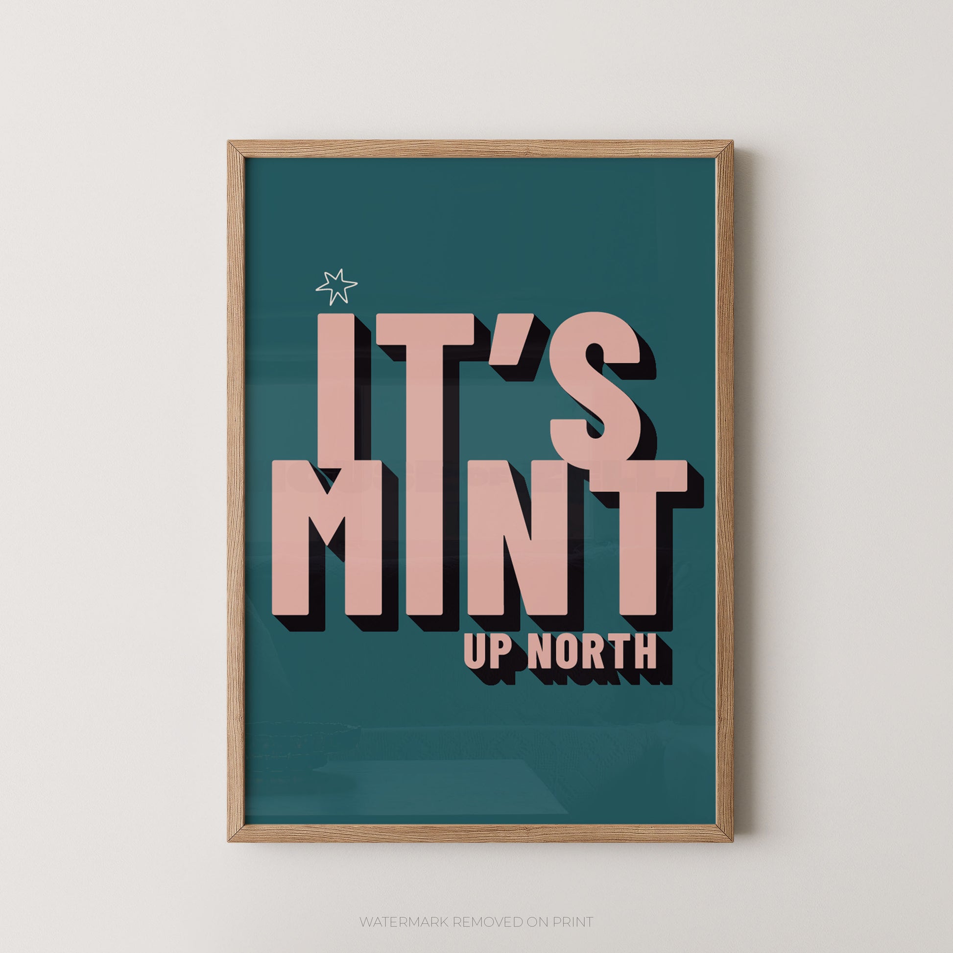 A framed typographic wall art print with the phrase “IT’S MINT UP NORTH” in large pink letters on a teal background, shown hanging against a light neutral wall.