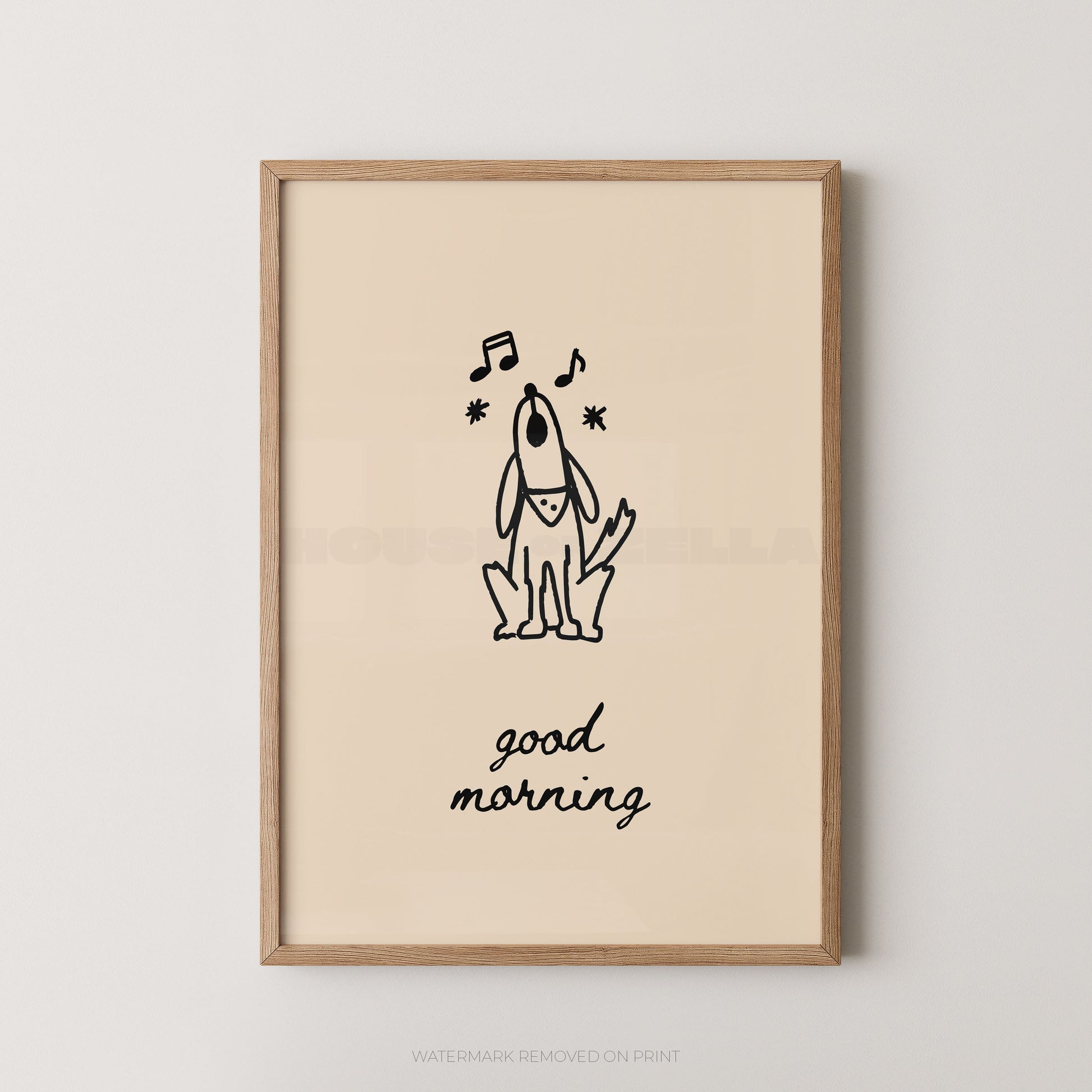 A framed art print featuring a minimalist black line drawing of a dog with musical notes and the text 'good morning' on a warm cream background, enclosed in a light natural wood frame against a neutral light gray wall.