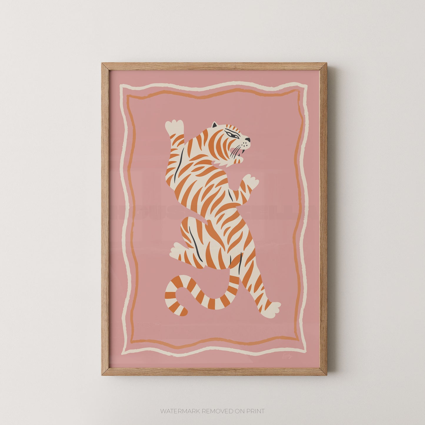 Framed wall art featuring a stylized orange and cream tiger on a dusty pink background, shown hanging against a light neutral wall.