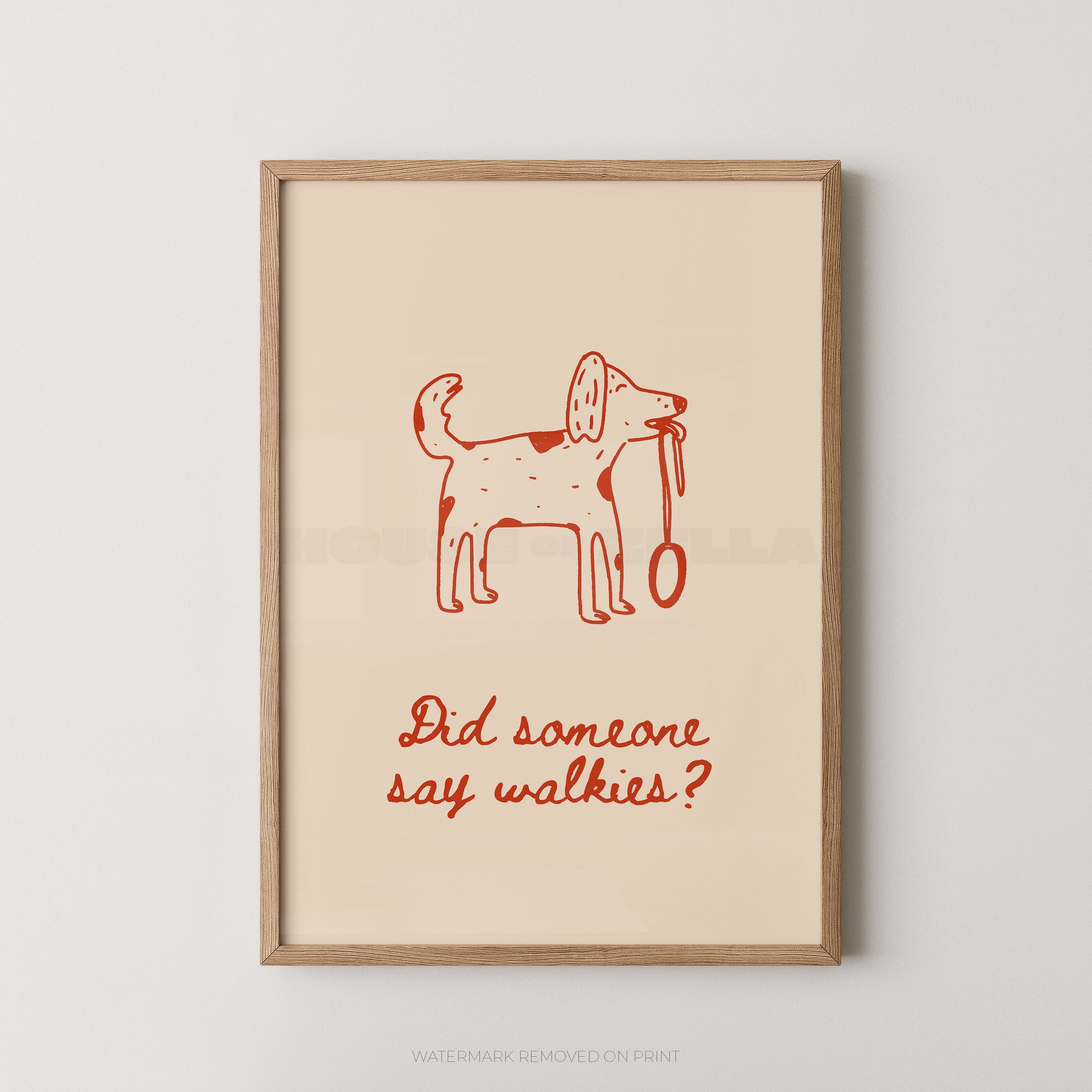 A framed art print featuring a minimalist red line drawing of a dog holding a leash on a warm cream background, with the text 'Did someone say walkies?' below. The print is housed in a light natural wood frame and is displayed against a neutral light gray wall.