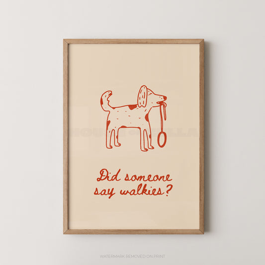 A framed art print featuring a minimalist red line drawing of a dog holding a leash on a warm cream background, with the text 'Did someone say walkies?' below. The print is housed in a light natural wood frame and is displayed against a neutral light gray wall.