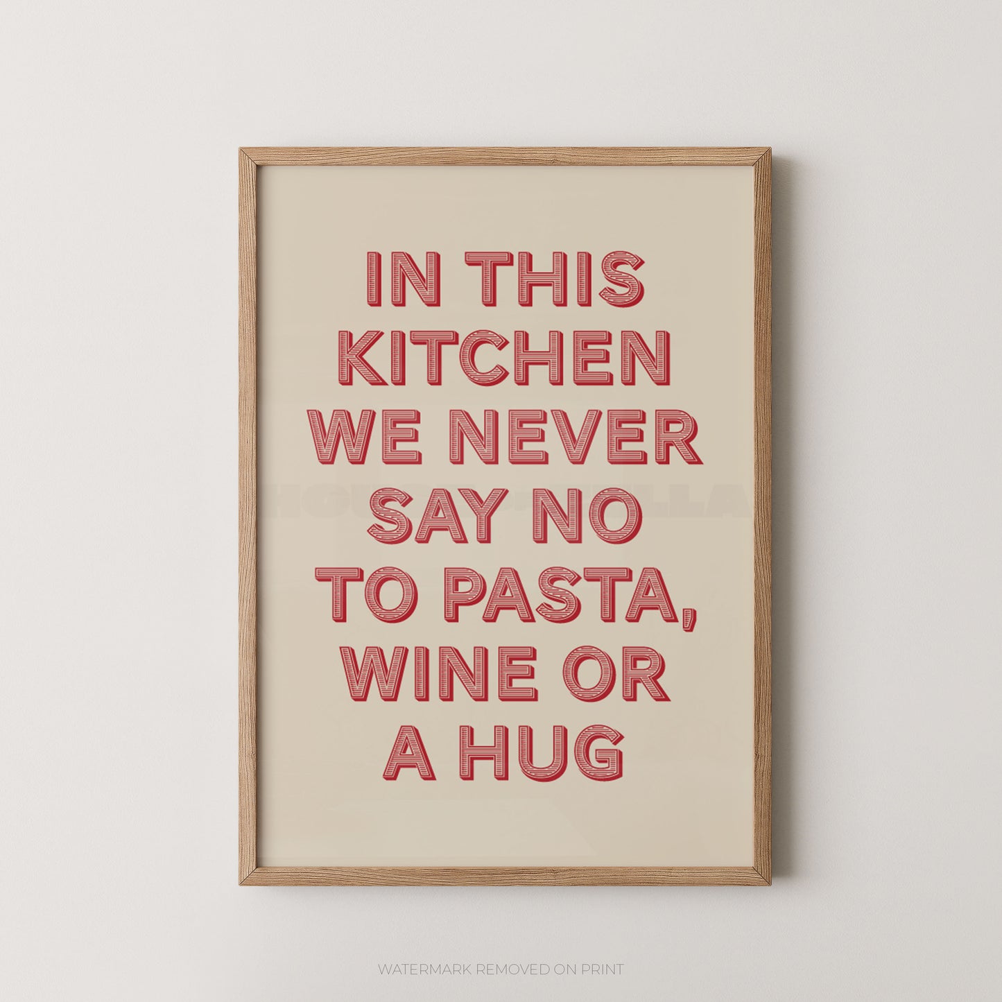A framed typographic wall art print with the phrase “IN THIS KITCHEN WE NEVER SAY NO TO PASTA, WINE OR A HUG” in raised coral-red letters on a warm cream background, shown against a light neutral wall.
