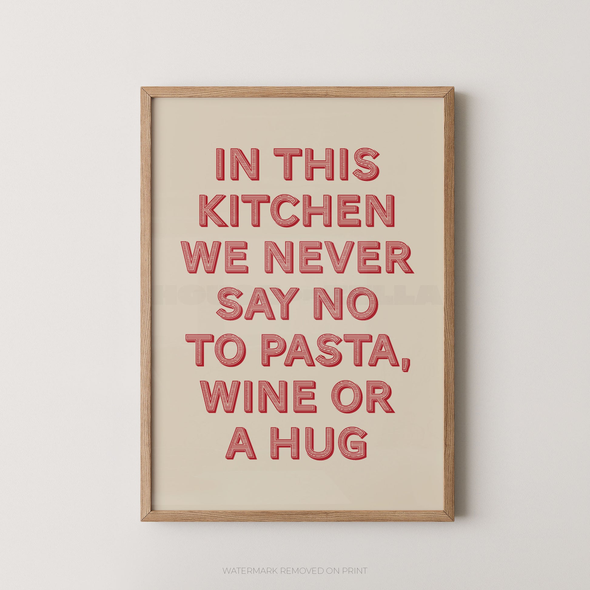 A framed typographic wall art print with the phrase “IN THIS KITCHEN WE NEVER SAY NO TO PASTA, WINE OR A HUG” in raised coral-red letters on a warm cream background, shown against a light neutral wall.