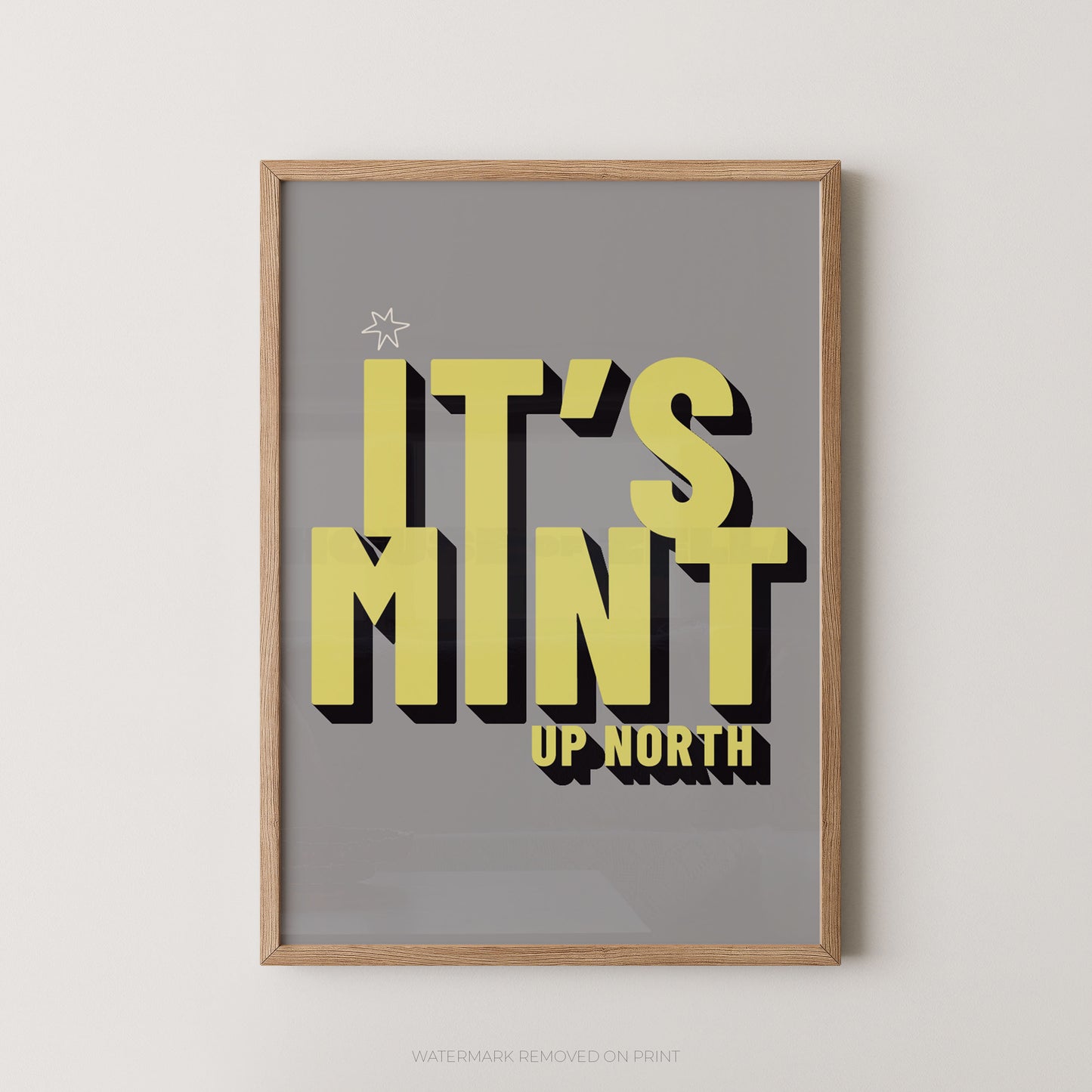 Framed typographic wall art reading “IT’S MINT UP NORTH” in large yellow letters with black drop shadows on a gray background, shown in a light wood frame against a light neutral wall.