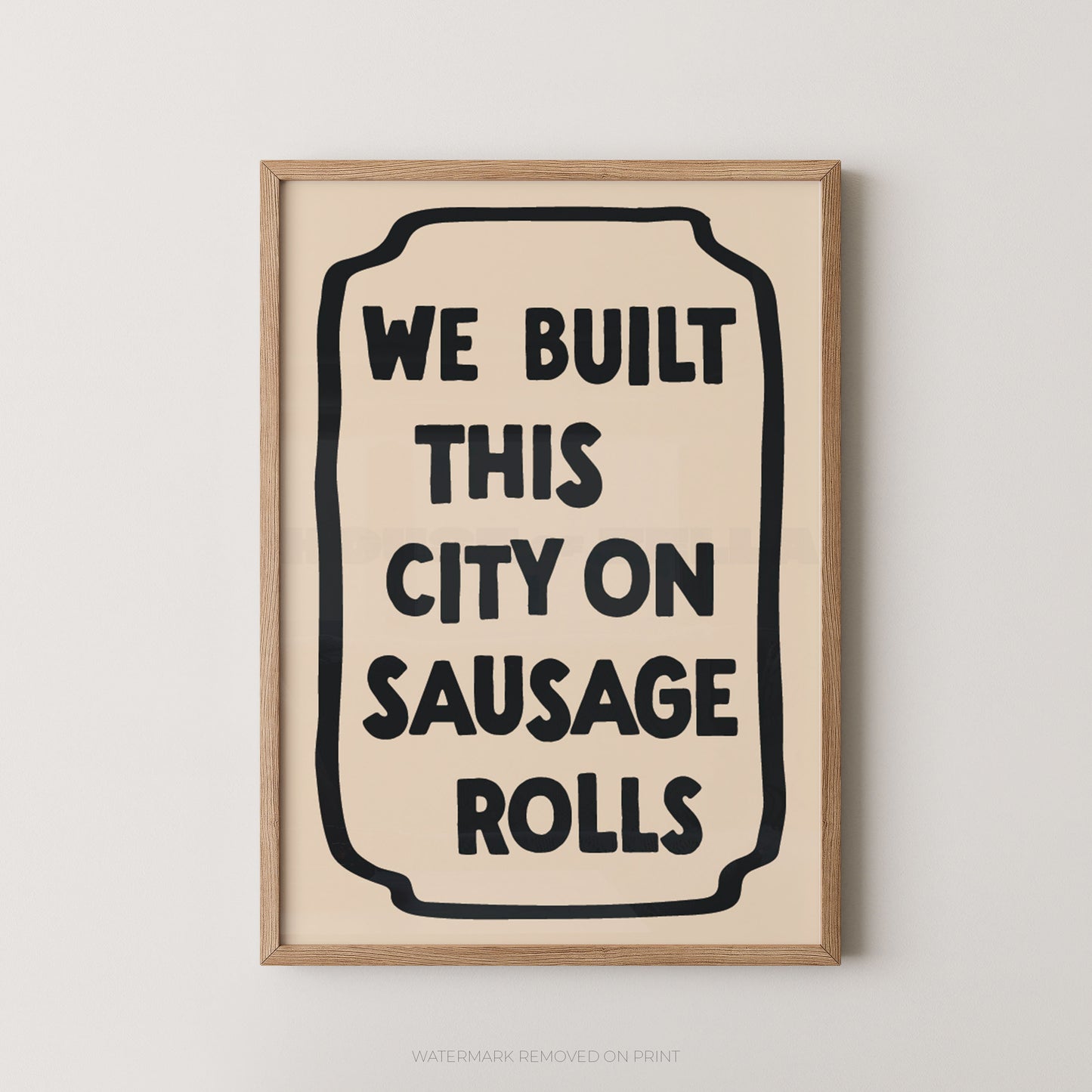 Framed wall art print with the phrase “WE BUILT THIS CITY ON SAUSAGE ROLLS” in bold black text inside a cream rectangle, set in a light natural wood frame against a light gray wall.