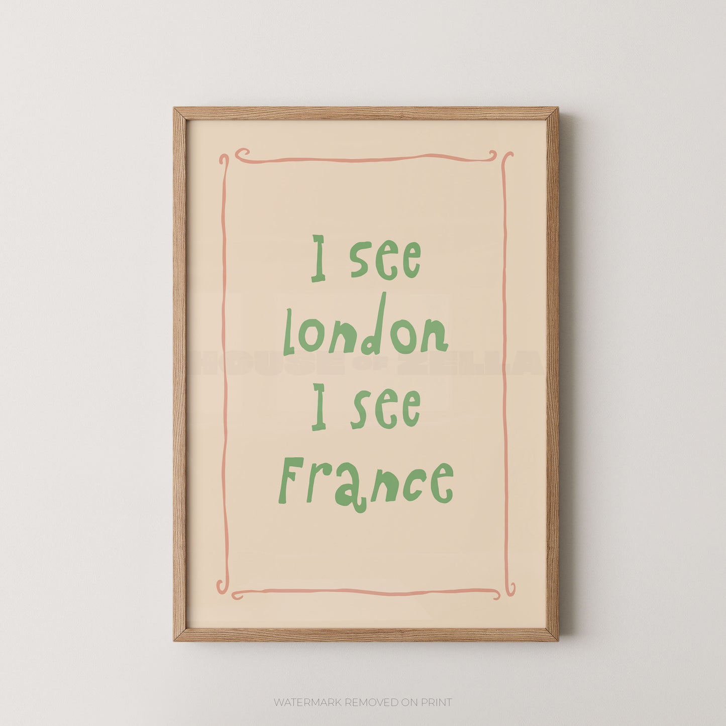 Framed typographic wall art print with the text 'I see London I see France' in green handwritten-style lettering on a warm cream background, bordered by a thin coral line and a light natural wood frame, shown against a light gray wall.