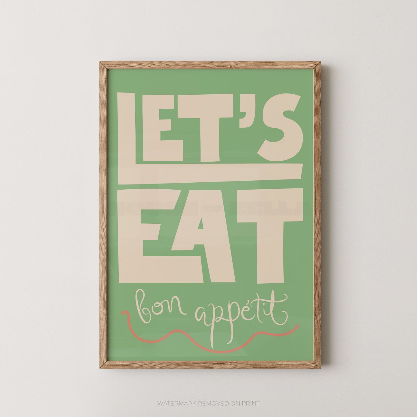 Framed wall art print with the phrase “LET’S EAT bon appetit” in cream lettering on a muted green background, shown hanging against a light neutral wall.