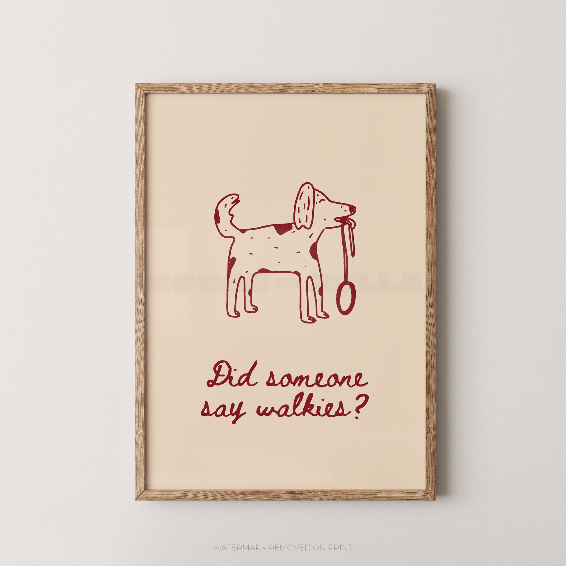 A framed art print featuring a simple red line drawing of a dog holding a leash on a warm cream background, with the text 'Did someone say walkies?' below. The print is housed in a light natural wood frame and is displayed against a neutral light gray wall.