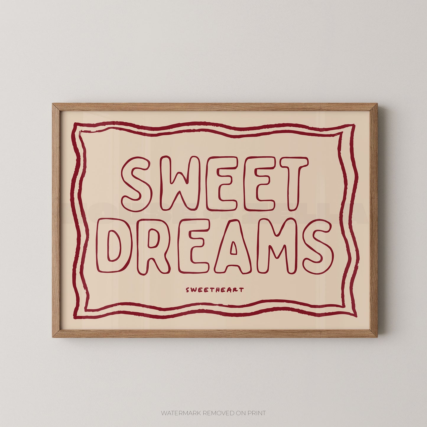 A framed typographic wall art print with the words “SWEET DREAMS” in large outlined red letters on a warm cream background, bordered by a wavy red line and shown in a light wood frame against a light gray wall.