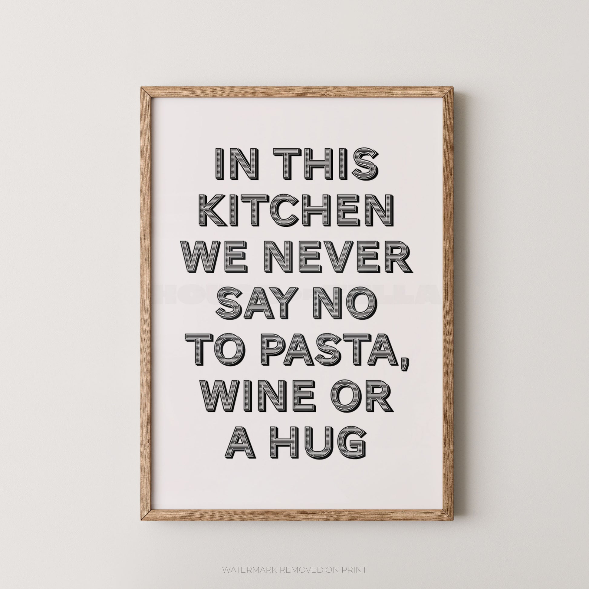 A framed typographic wall art print with the phrase “IN THIS KITCHEN WE NEVER SAY NO TO PASTA, WINE OR A HUG” in large gray letters on a white background, shown hanging against a light gray wall.