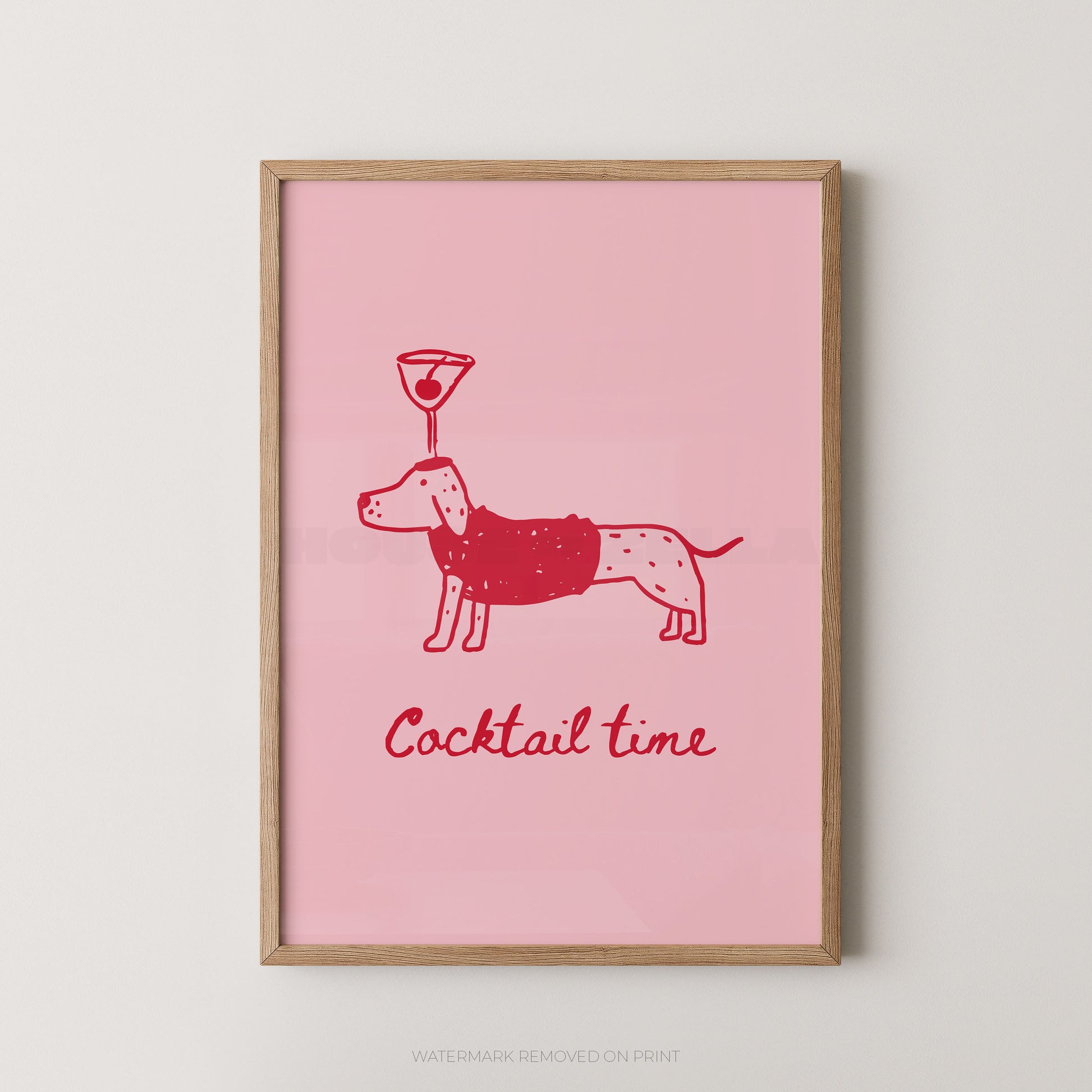 A framed art print featuring a pink background with a red line drawing of a dachshund wearing a sweater and balancing a cocktail glass on its head, with the text 'Cocktail time' below. The print is housed in a light natural wood frame and is displayed against a neutral light gray wall.