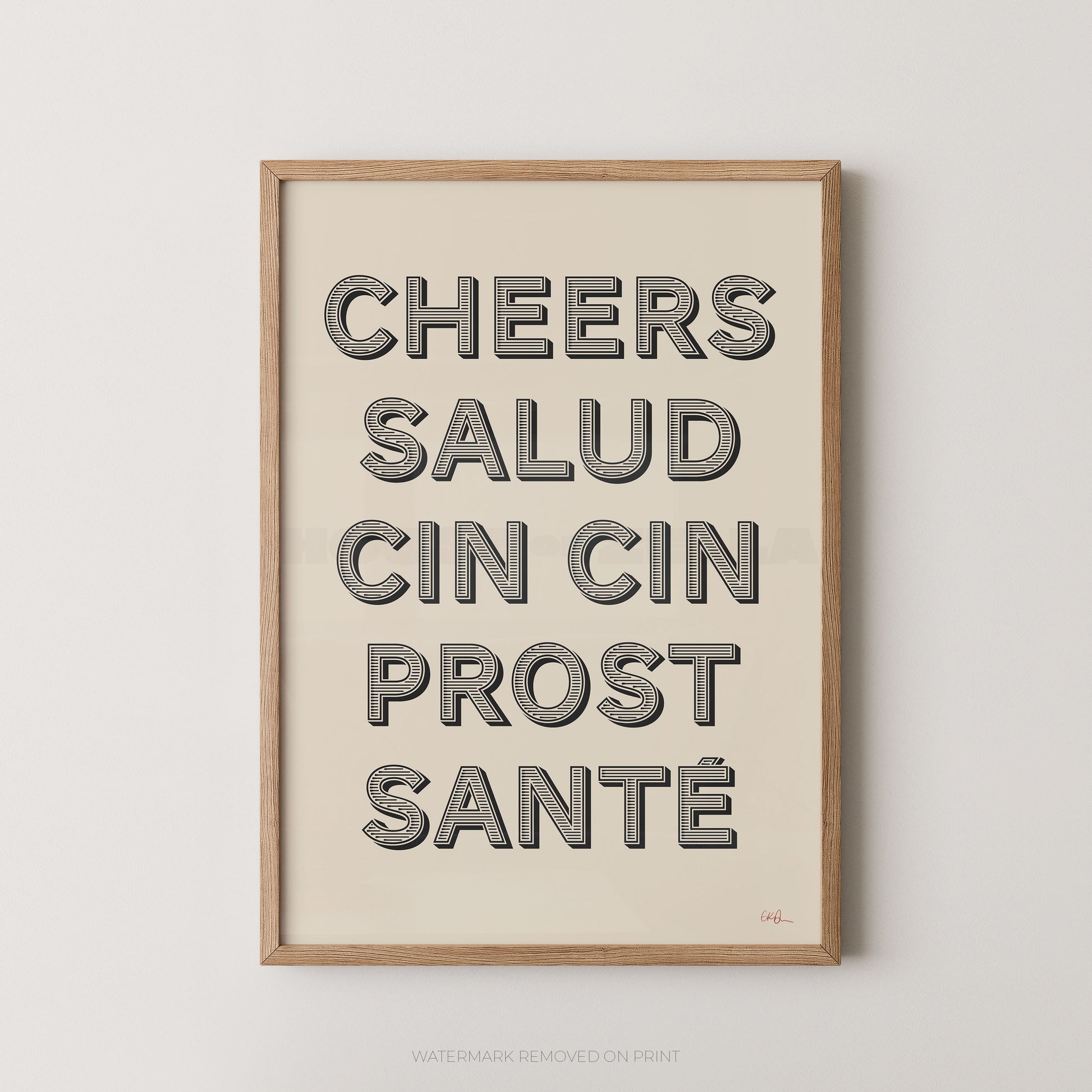 A framed typographic wall art print with the words 'CHEERS SALUD CIN CIN PROST SANTÉ' in large gray letters on a warm cream background, shown hanging against a light gray wall.
