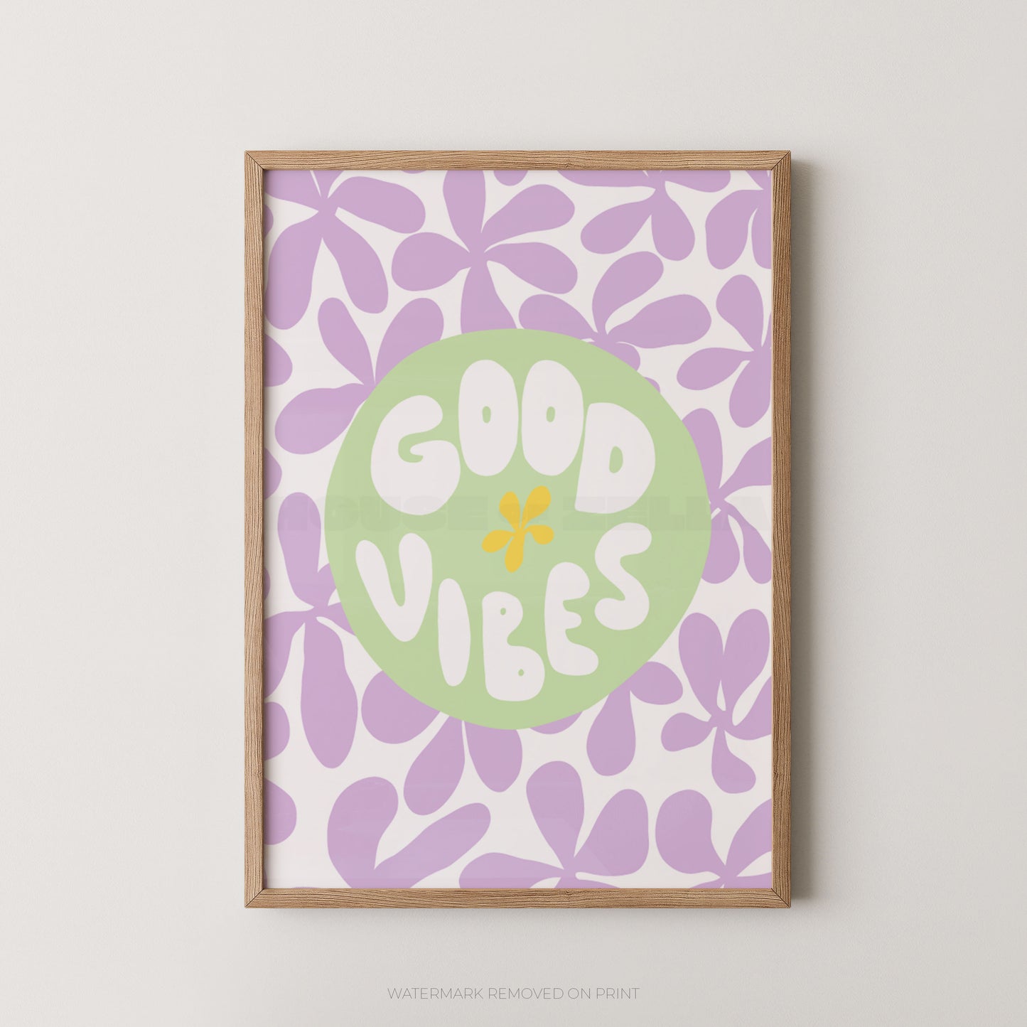 A framed art print featuring a retro floral pattern in lavender and white, with a central light green circle containing the words 'GOOD VIBES' in white letters and a small yellow flower accent. The print is housed in a light natural wood frame and is displayed against a neutral light gray wall.