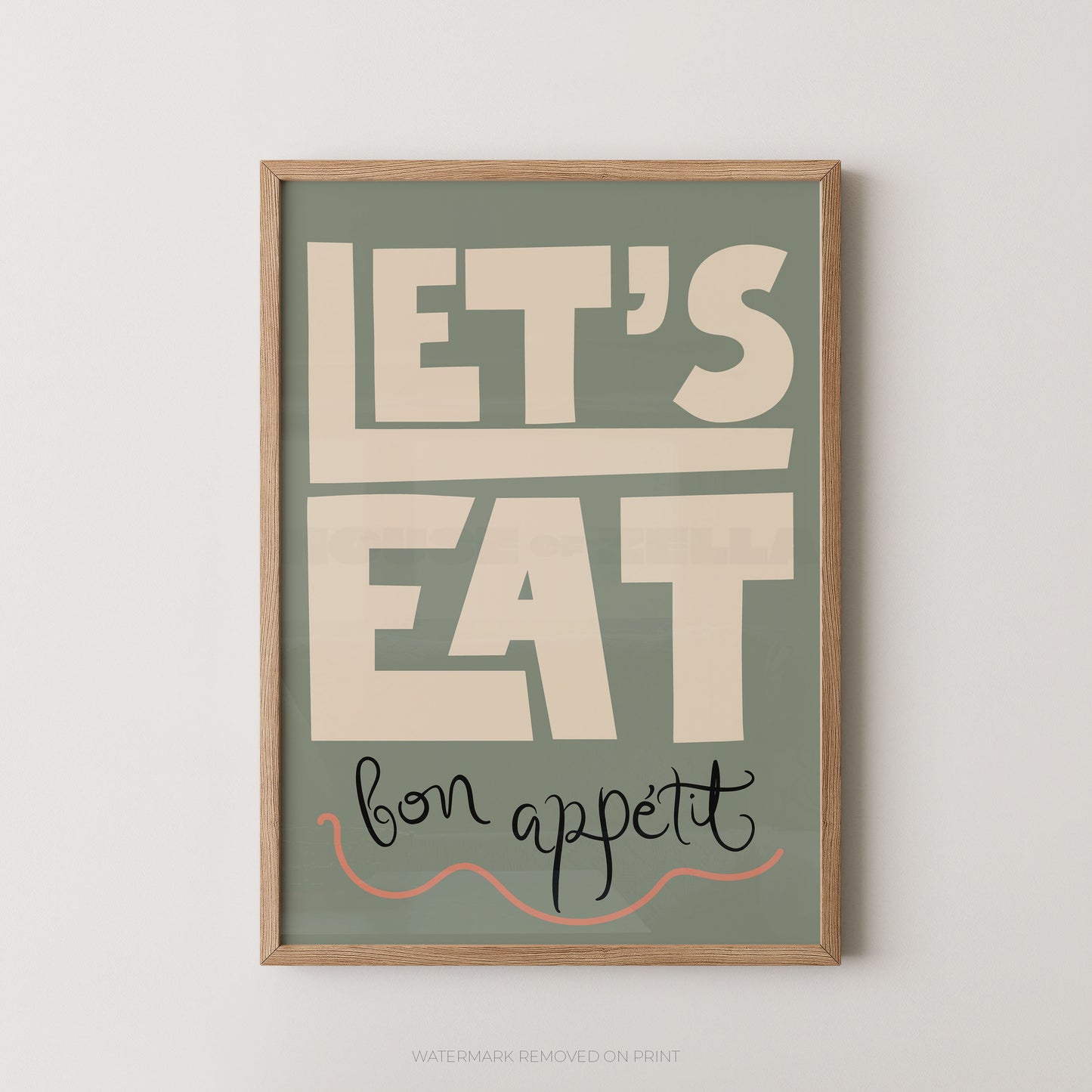 Framed wall art print with the phrase “LET’S EAT bon appetit” in large cream lettering on a muted sage green background, shown in a light wood frame against a white wall.