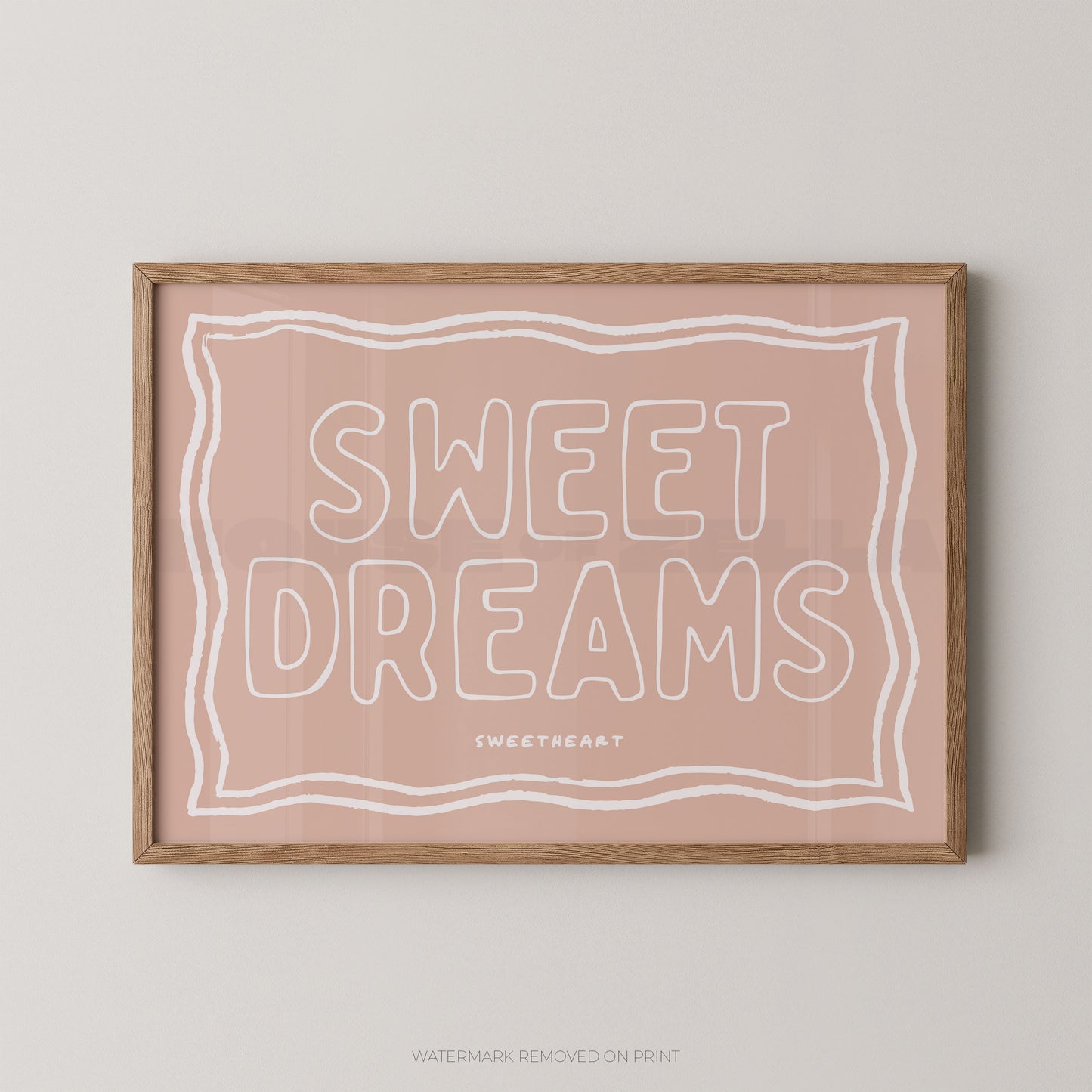 A framed art print with the words 'SWEET DREAMS' in white outline lettering on a dusty pink background, enclosed in a light natural wood frame and mounted on a light gray wall.