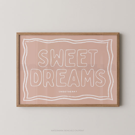 A framed art print with the words 'SWEET DREAMS' in white outline lettering on a dusty pink background, enclosed in a light natural wood frame and mounted on a light gray wall.