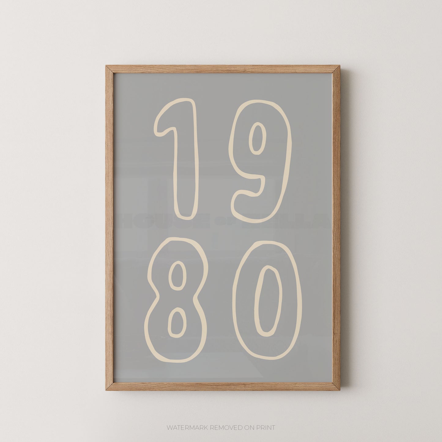 Framed wall art print with the numbers '1980' in cream outlined font on a light gray background, shown in a natural wood frame against a white wall.