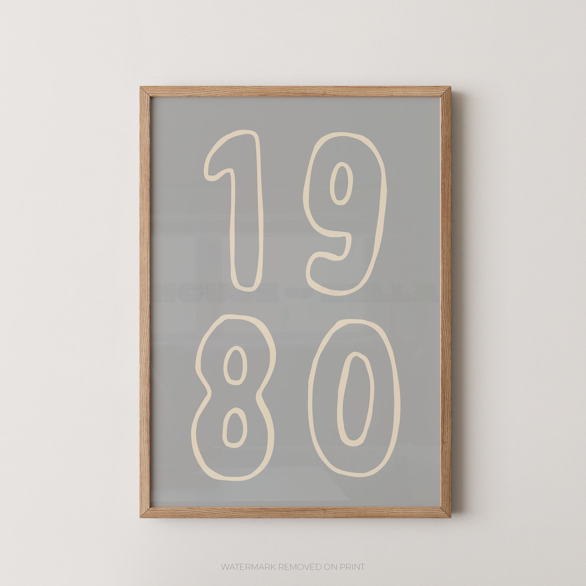 Framed wall art print with the numbers '1980' in cream outlined font on a light gray background, shown in a natural wood frame against a white wall.