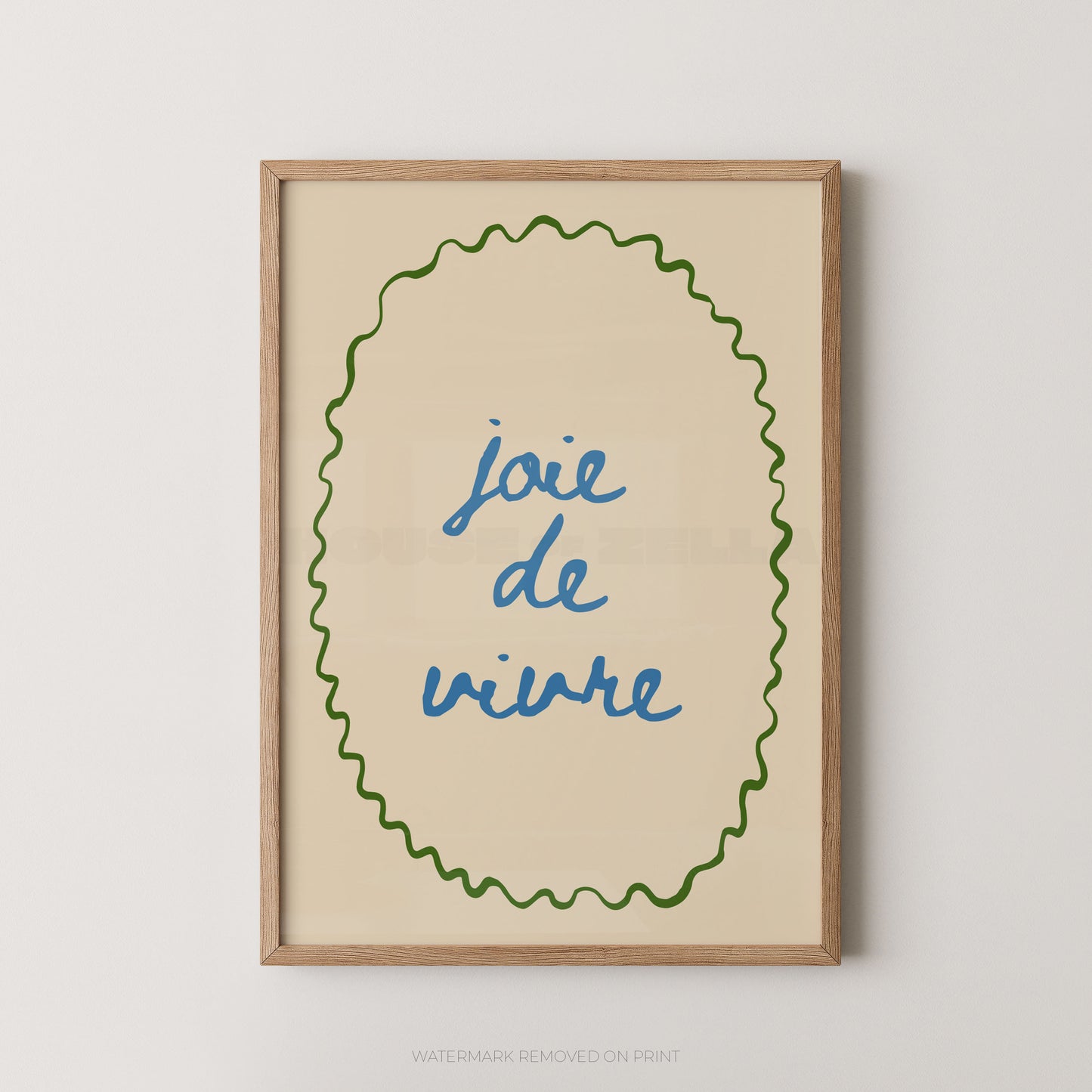 Framed wall art print with the French phrase “joie de vivre” in blue script inside a green wavy oval border on a warm cream background, shown in a light wood frame against a light gray wall.