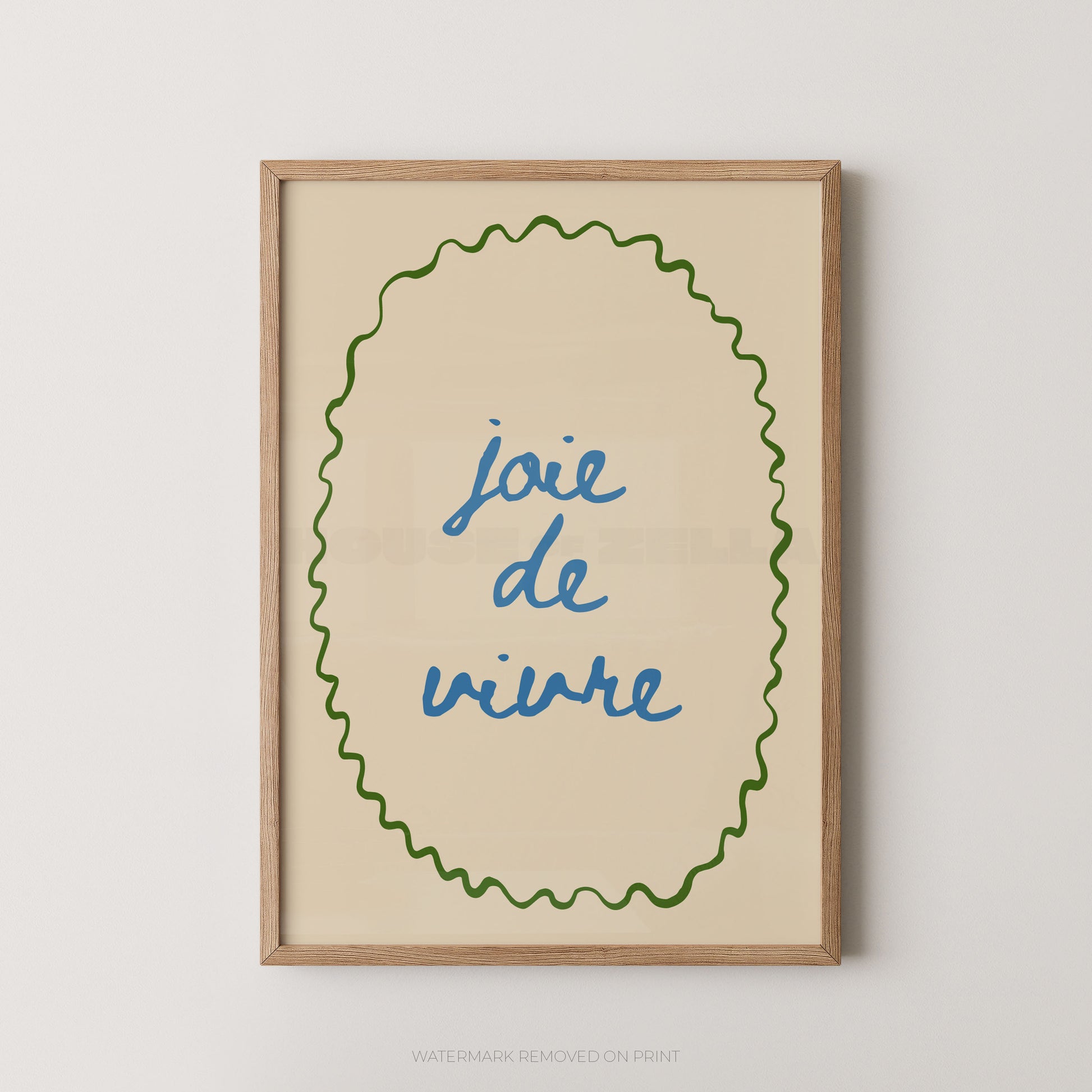 Framed wall art print with the French phrase “joie de vivre” in blue script inside a green wavy oval border on a warm cream background, shown in a light wood frame against a light gray wall.