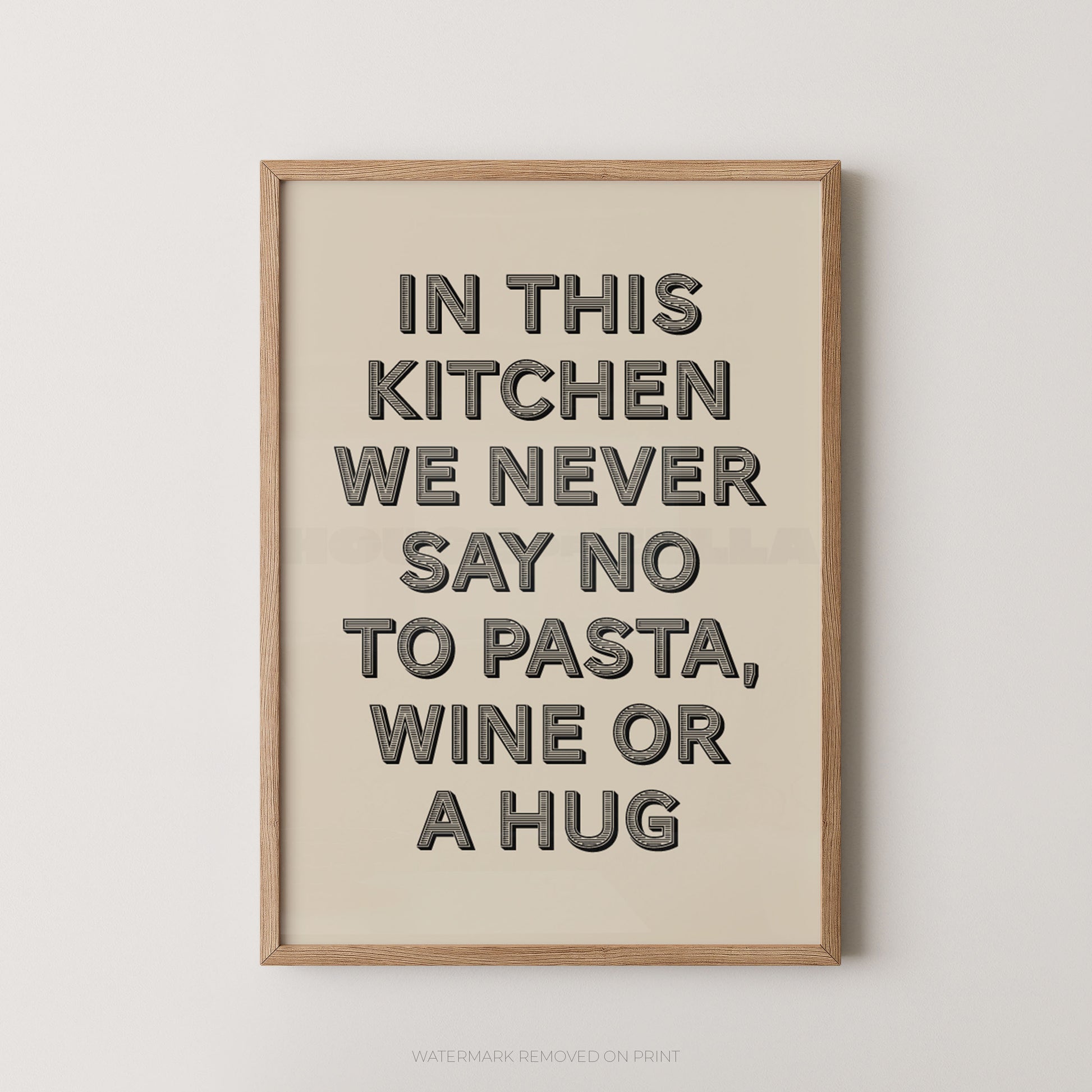 A framed typographic wall art print with the phrase “IN THIS KITCHEN WE NEVER SAY NO TO PASTA, WINE OR A HUG” in dark gray letters on a warm cream background, shown hanging against a light neutral wall.
