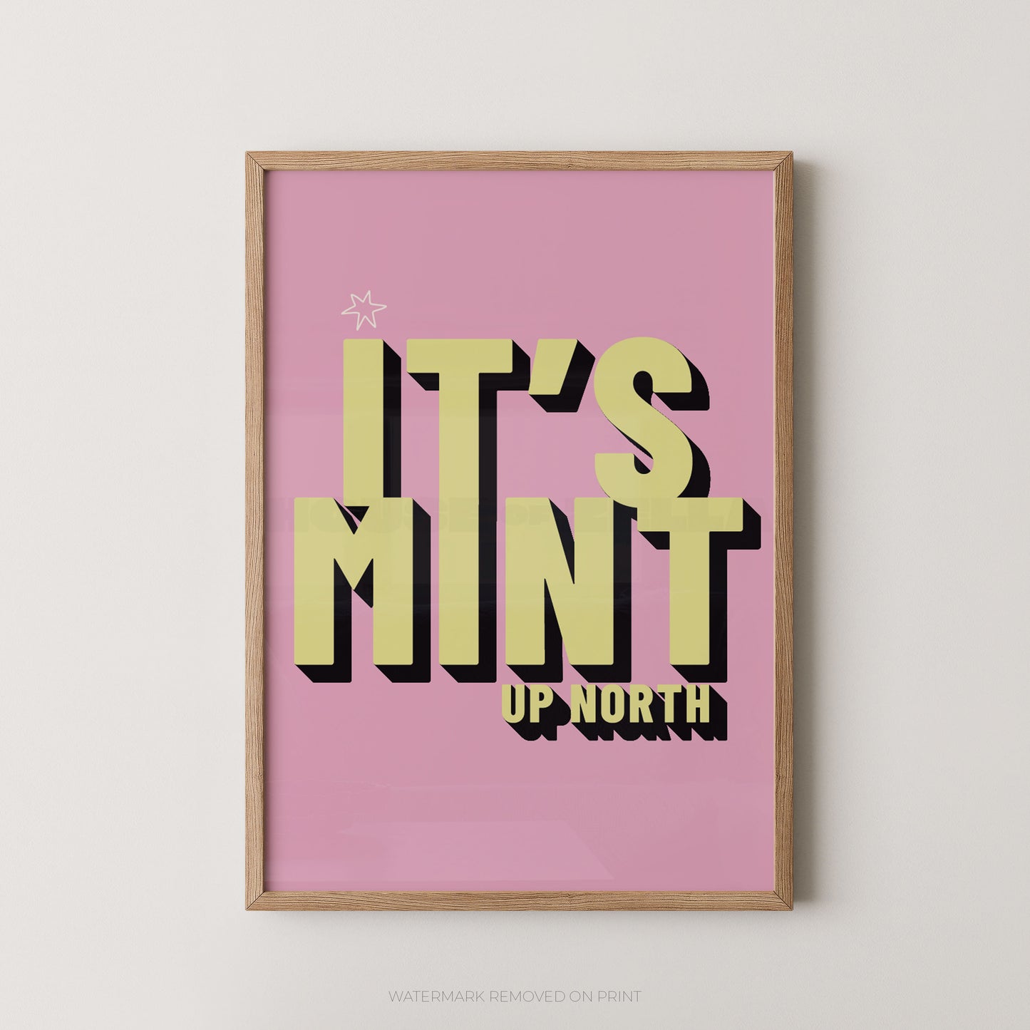 Framed typographic wall art with the phrase “IT’S MINT UP NORTH” in large yellow-green letters with black drop shadows on a pink background, shown hanging against a light neutral wall.
