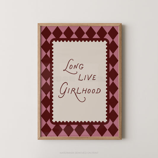 A framed art print featuring the text 'Long Live Girlhood' in dark red script on a cream background, surrounded by a pink and dark red diamond pattern, in a light wood frame.