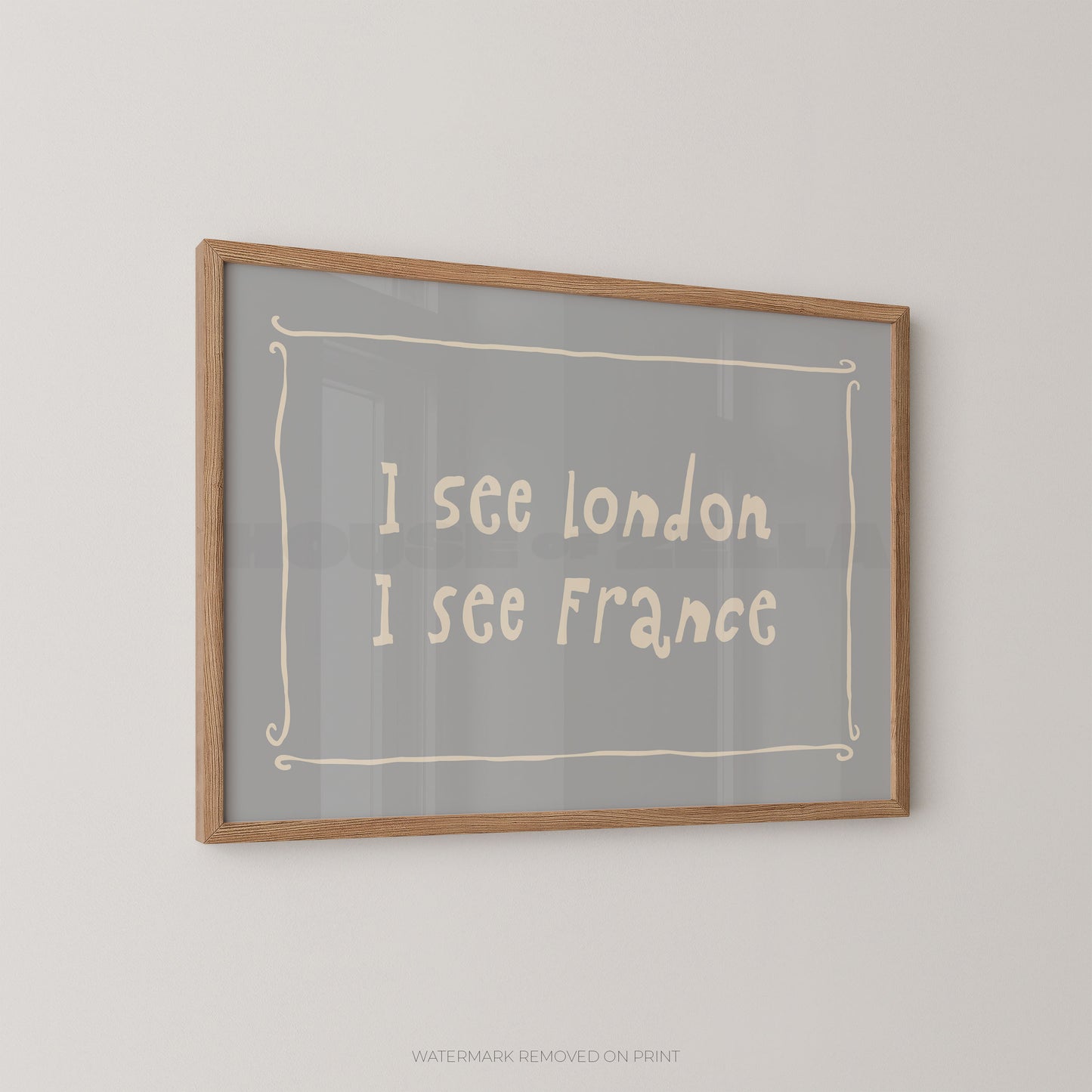 Framed wall art print with the text 'I see London I see France' in a light cream handwritten font on a gray background, enclosed in a natural wood frame and mounted on a light gray wall.