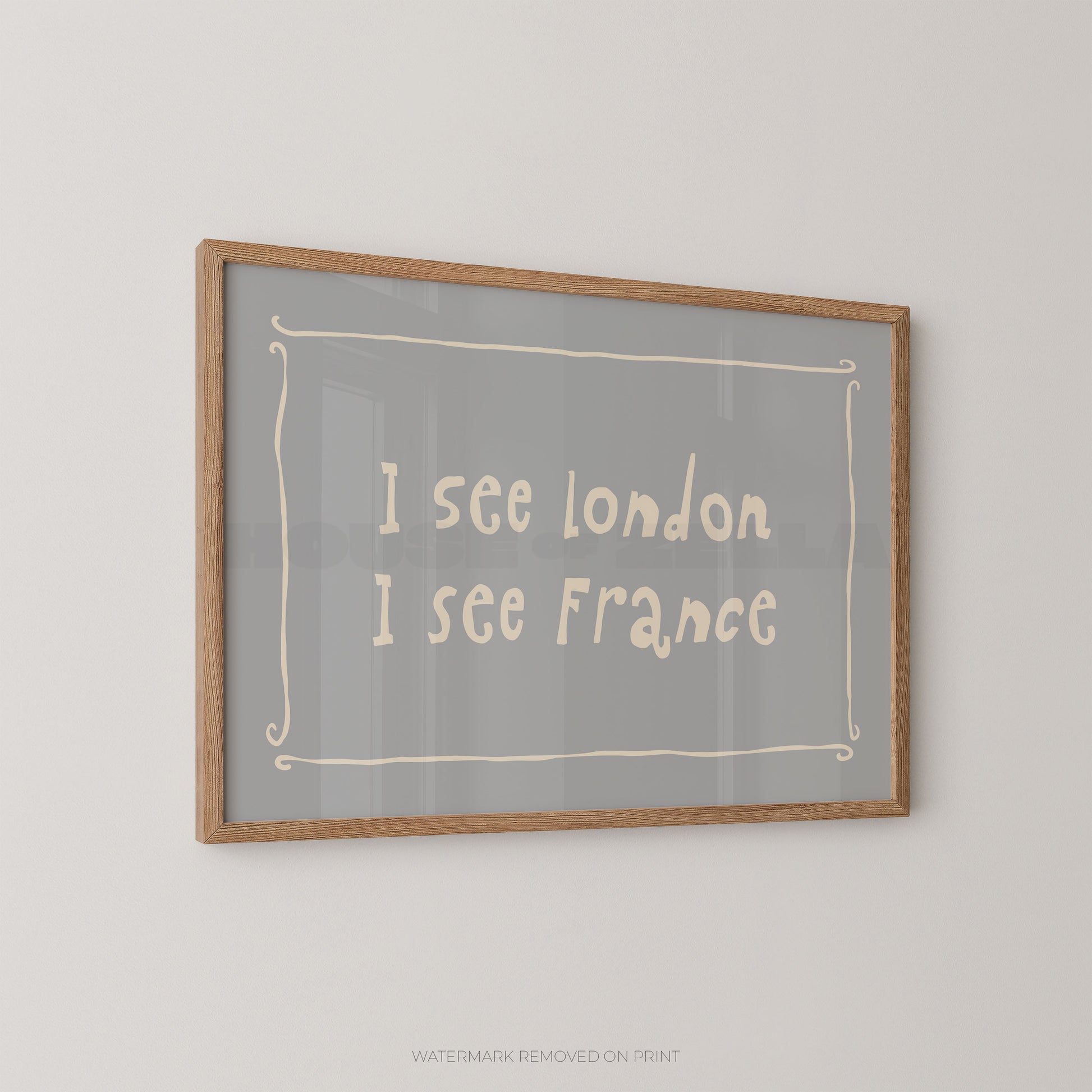 Framed wall art print with the text 'I see London I see France' in a light cream handwritten font on a gray background, enclosed in a natural wood frame and mounted on a light gray wall.